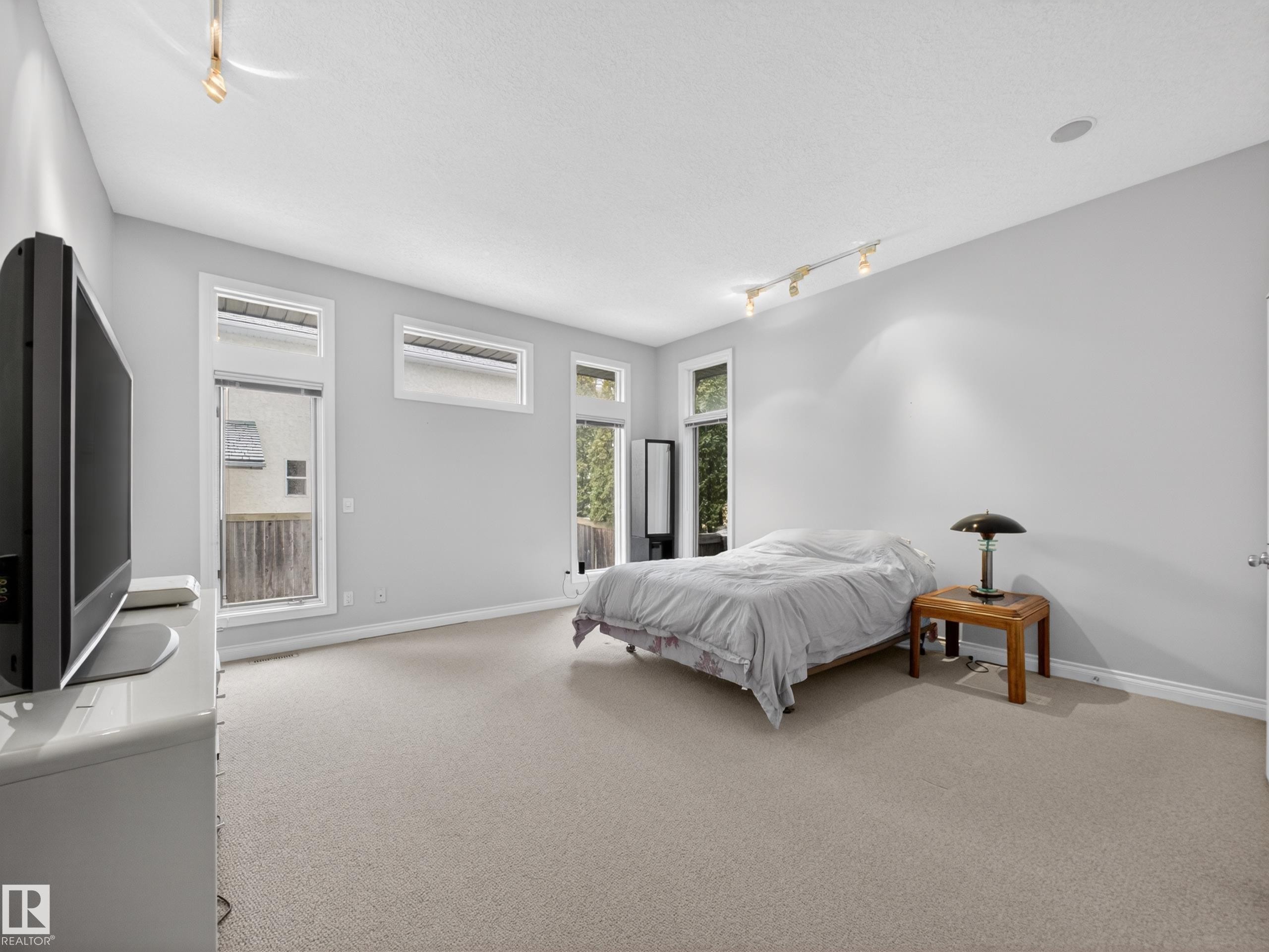 Carpeted room featuring multiple windows with white trim, track lighting, and a built-in ceiling speaker - 569 Butterworth Way, Edmonton, AB - Indoor Photo Showing Bedroom
