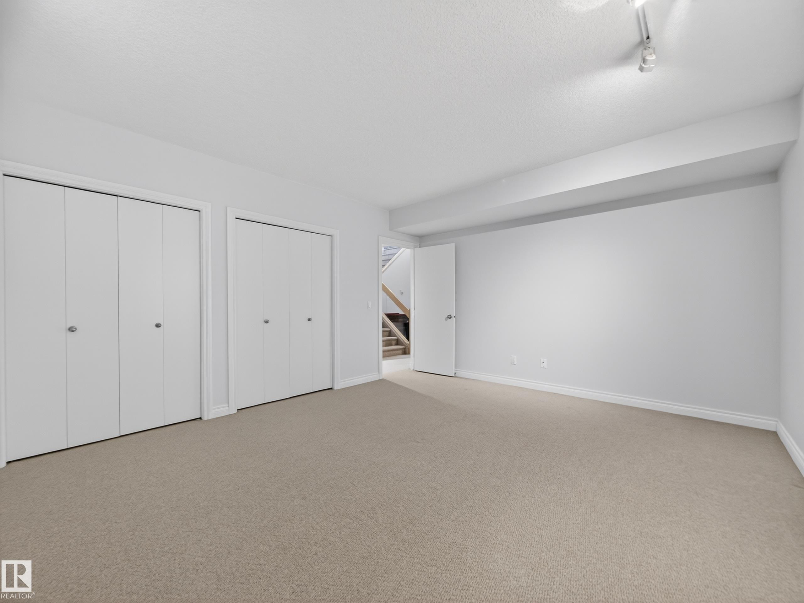 Spacious room featuring neutral carpet flooring, two sets of white bi-fold closet doors, and white painted walls - 569 Butterworth Way, Edmonton, AB - Indoor Photo Showing Other Room