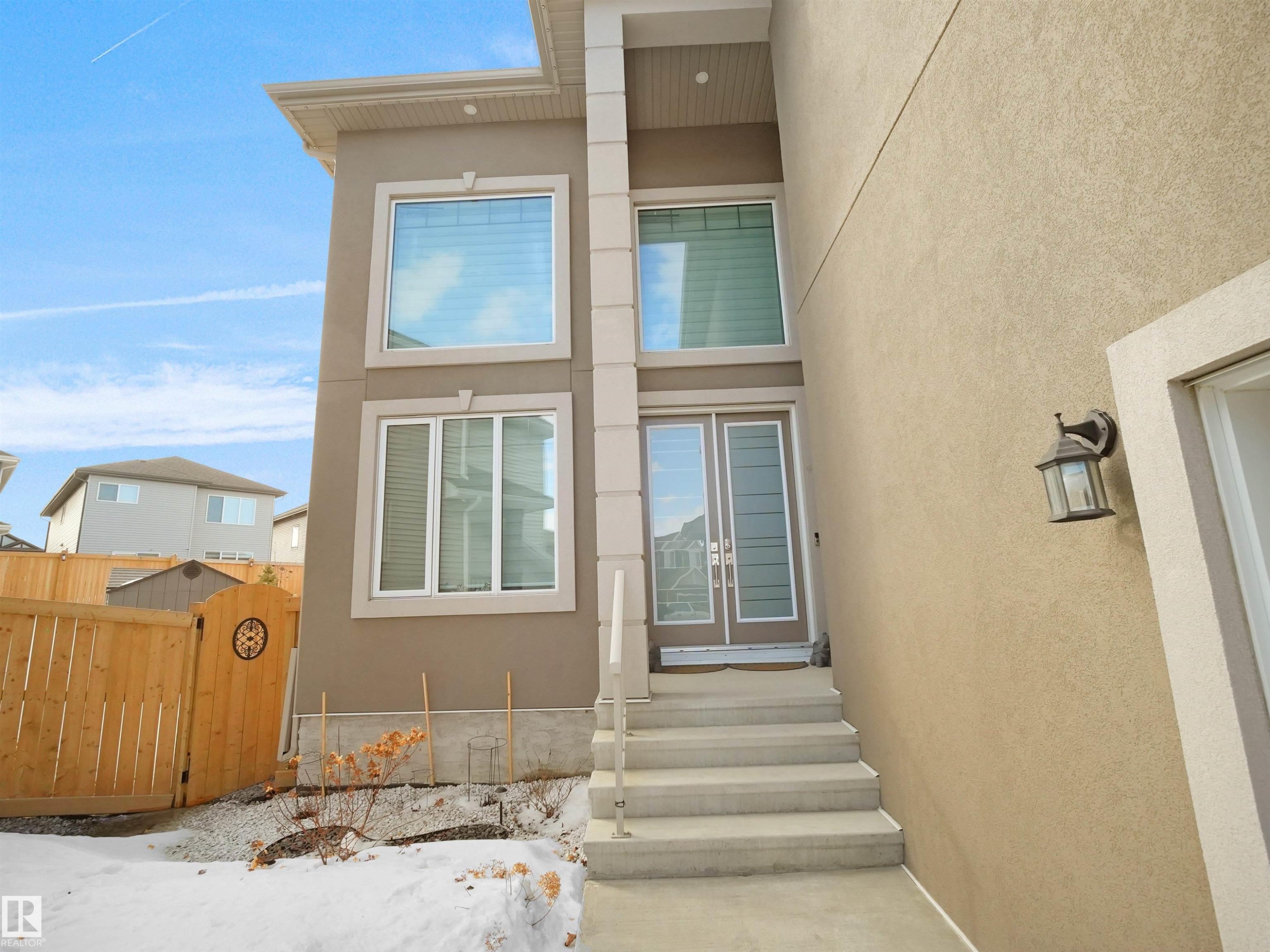 Contemporary stucco exterior with a tall entryway, featuring a double glass panel door and upper transom window - 1208 25 St Nw, Edmonton, AB - Outdoor