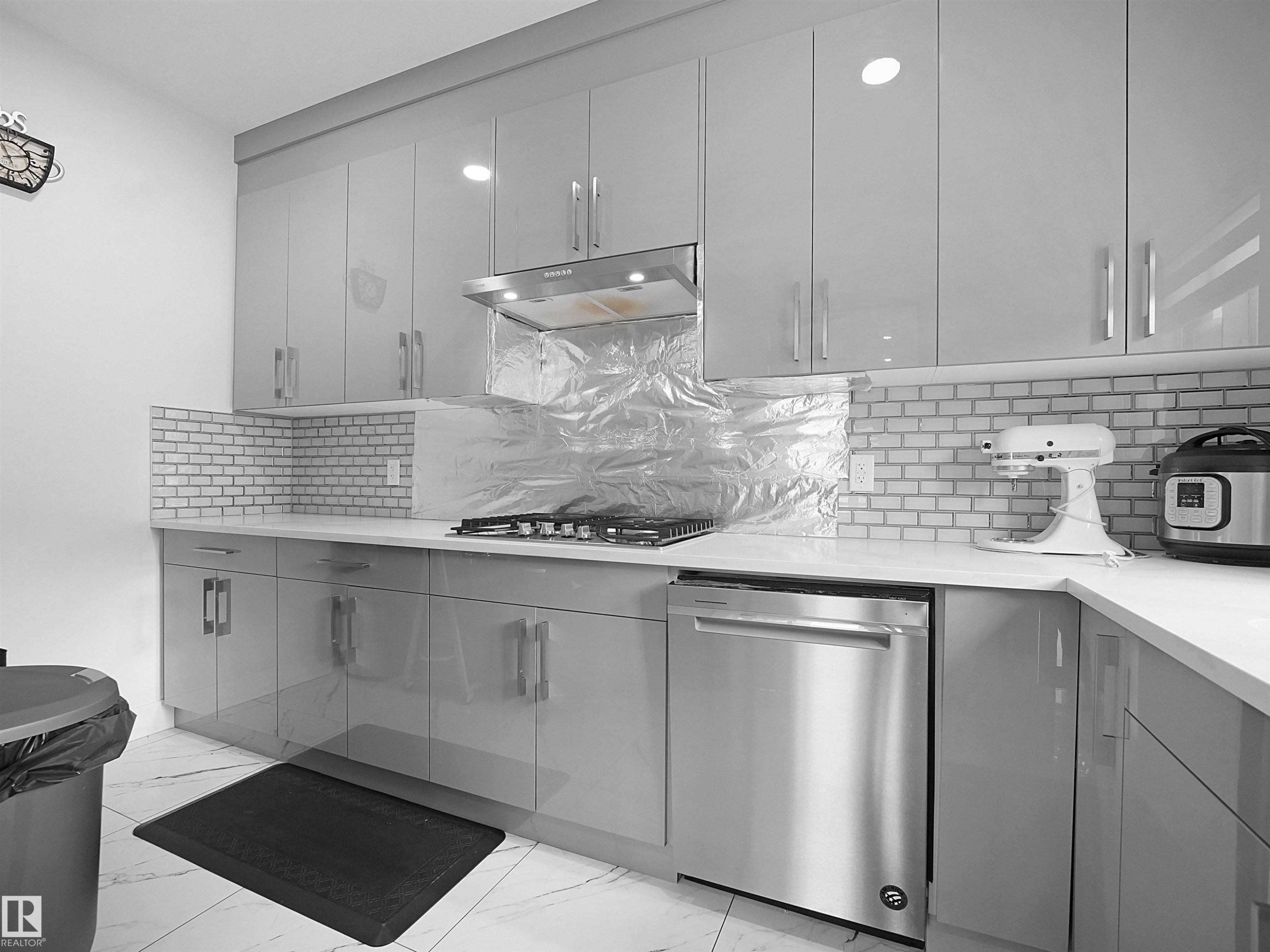 Contemporary kitchen featuring light gray high-gloss cabinetry, white countertop surfaces, a subway tile backsplash, stainless steel dishwasher, and a built-in range hood - 1208 25 St Nw, Edmonton, AB - Indoor Photo Showing Kitchen With Upgraded Kitchen