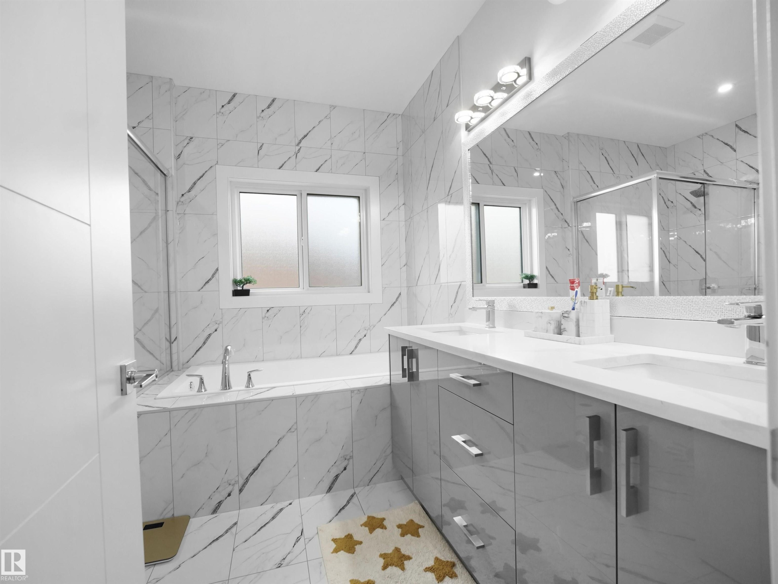Full bathroom featuring a built-in tub, white marble-look wall and floor tile, a dual vanity with a white countertop and grey cabinetry, and a glass-enclosed shower - 1208 25 St Nw, Edmonton, AB - Indoor Photo Showing Bathroom