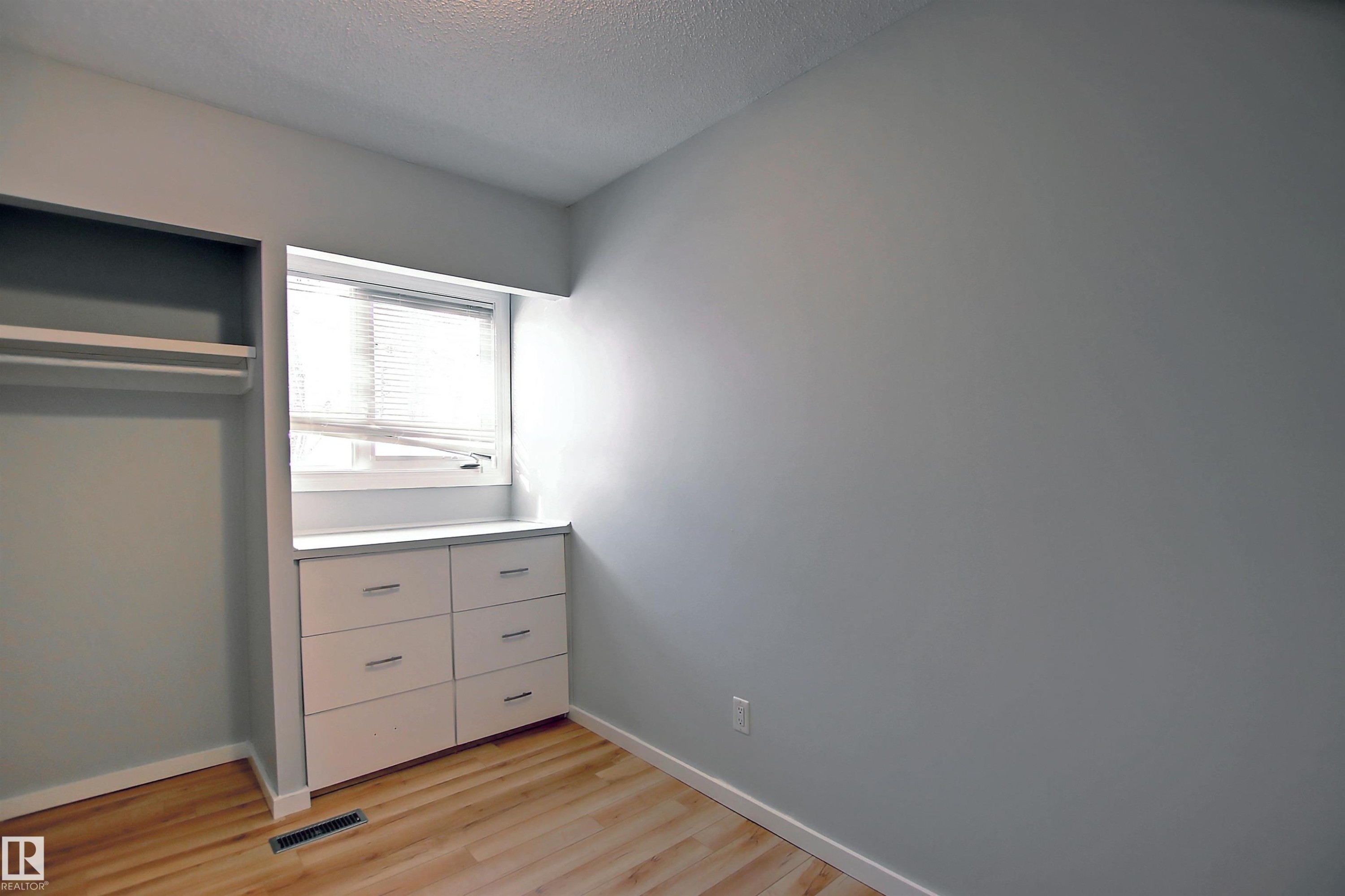 Room featuring wood-finish flooring, light gray wall paint, and a built-in storage unit with six drawers - 11 14120 80 Street, Edmonton, AB - Indoor
