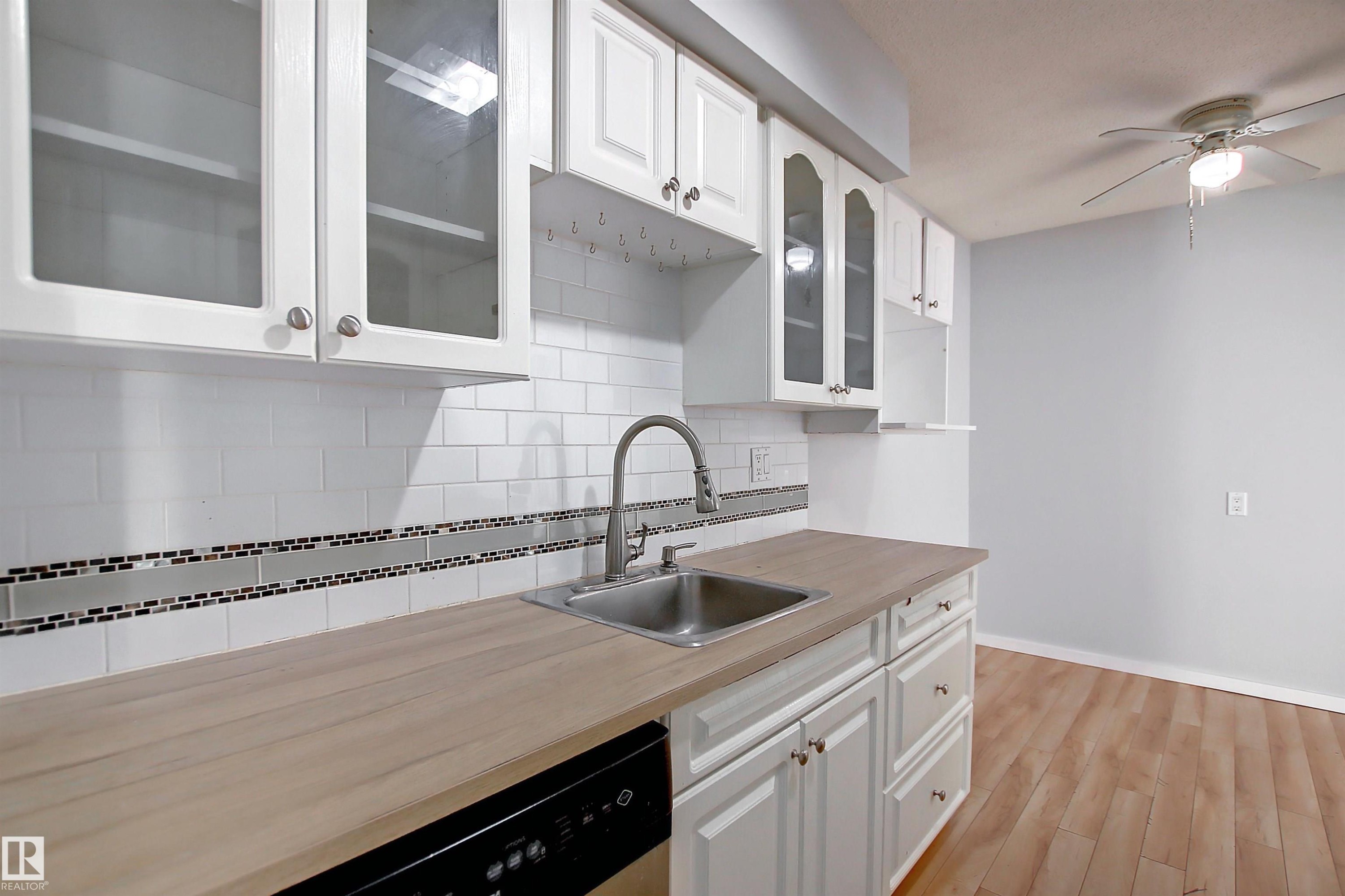 Kitchen featuring wood-finish countertops, stainless steel sink with a high-arc faucet, and white subway tile backsplash with a decorative mosaic accent - 11 14120 80 Street, Edmonton, AB - Indoor Photo Showing Kitchen