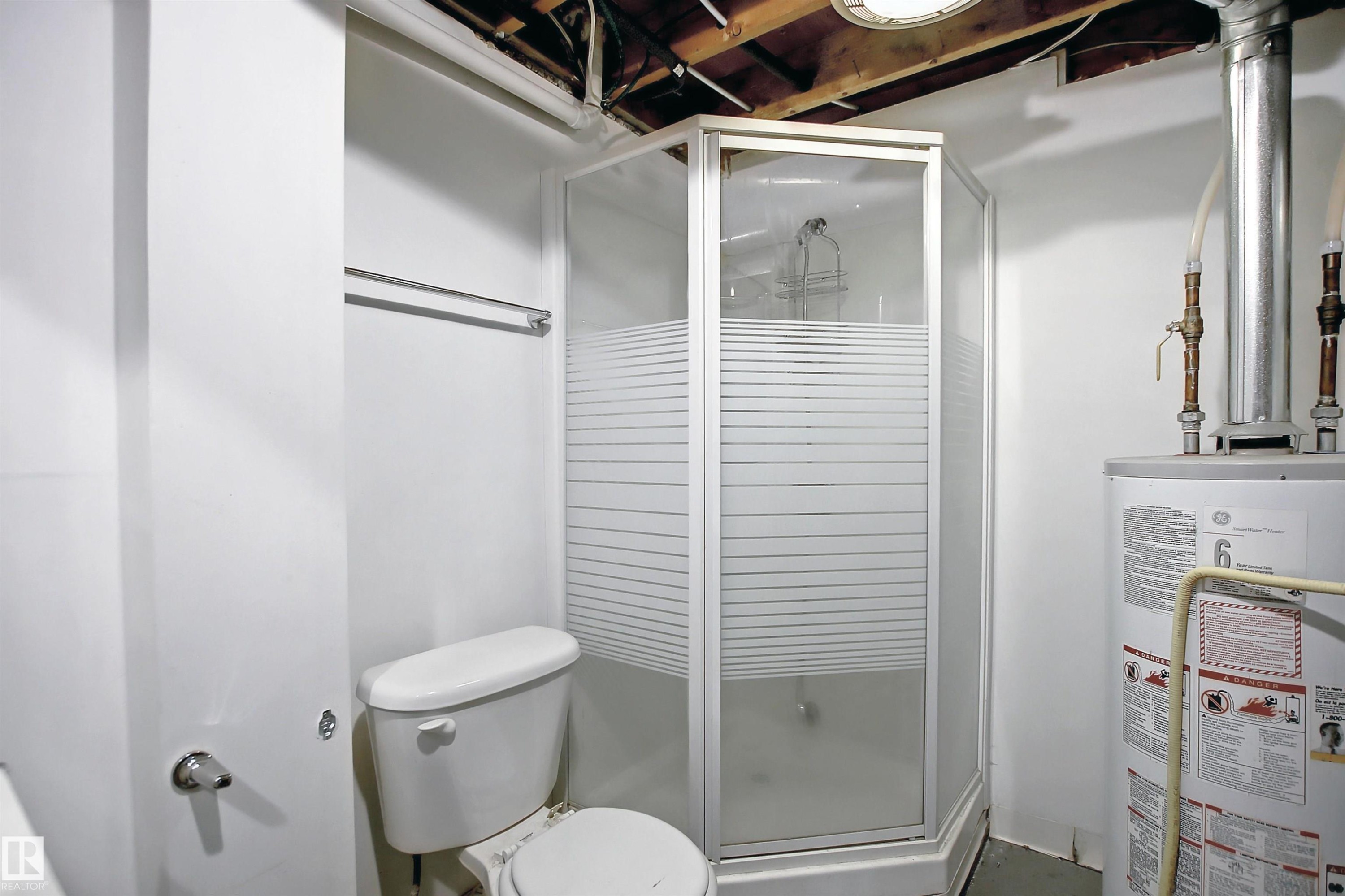 Compact bathroom featuring a corner shower with frosted glass panels, a white toilet, and exposed ceiling joists - 11 14120 80 Street, Edmonton, AB - Indoor Photo Showing Bathroom