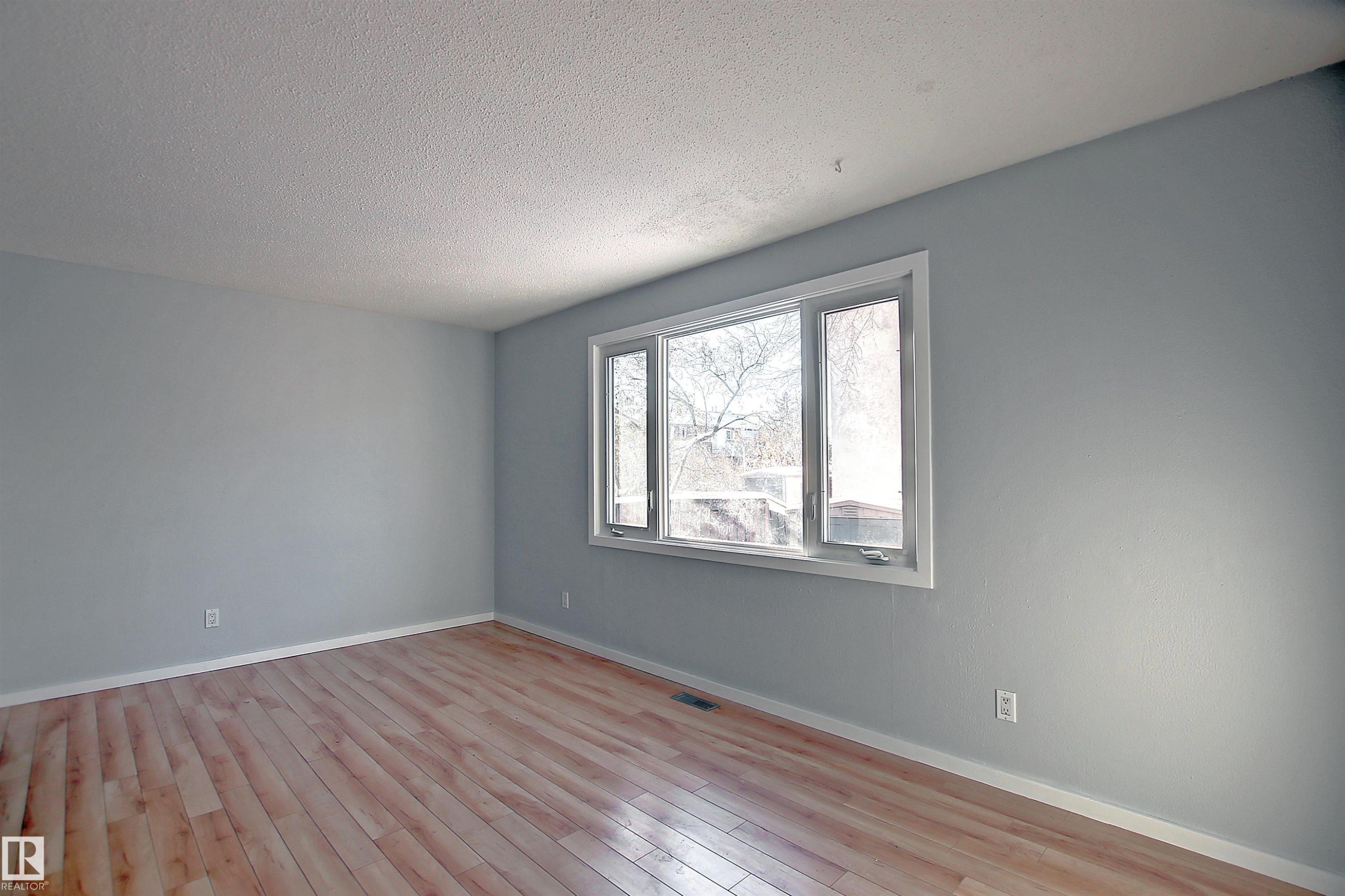 Bright interior space featuring a multi-pane window with white trim, light-toned wood-finish flooring, light gray walls, and white baseboards - 11 14120 80 Street, Edmonton, AB - Indoor Photo Showing Other Room