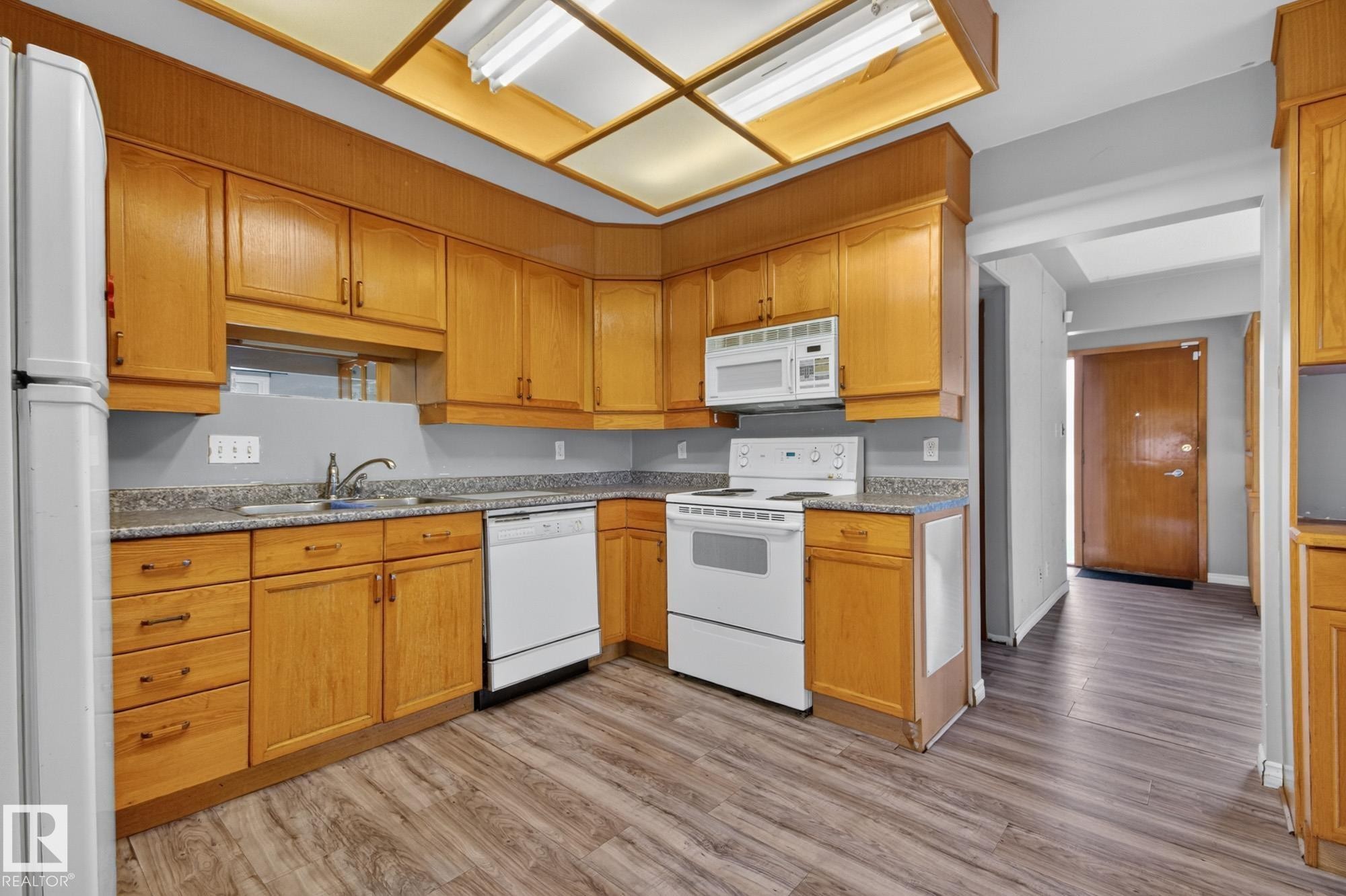 Kitchen featuring wood-finish cabinetry, light-toned countertops, and wood-finish flooring - 11901 42 Street Nw, Edmonton, AB - Indoor Photo Showing Kitchen
