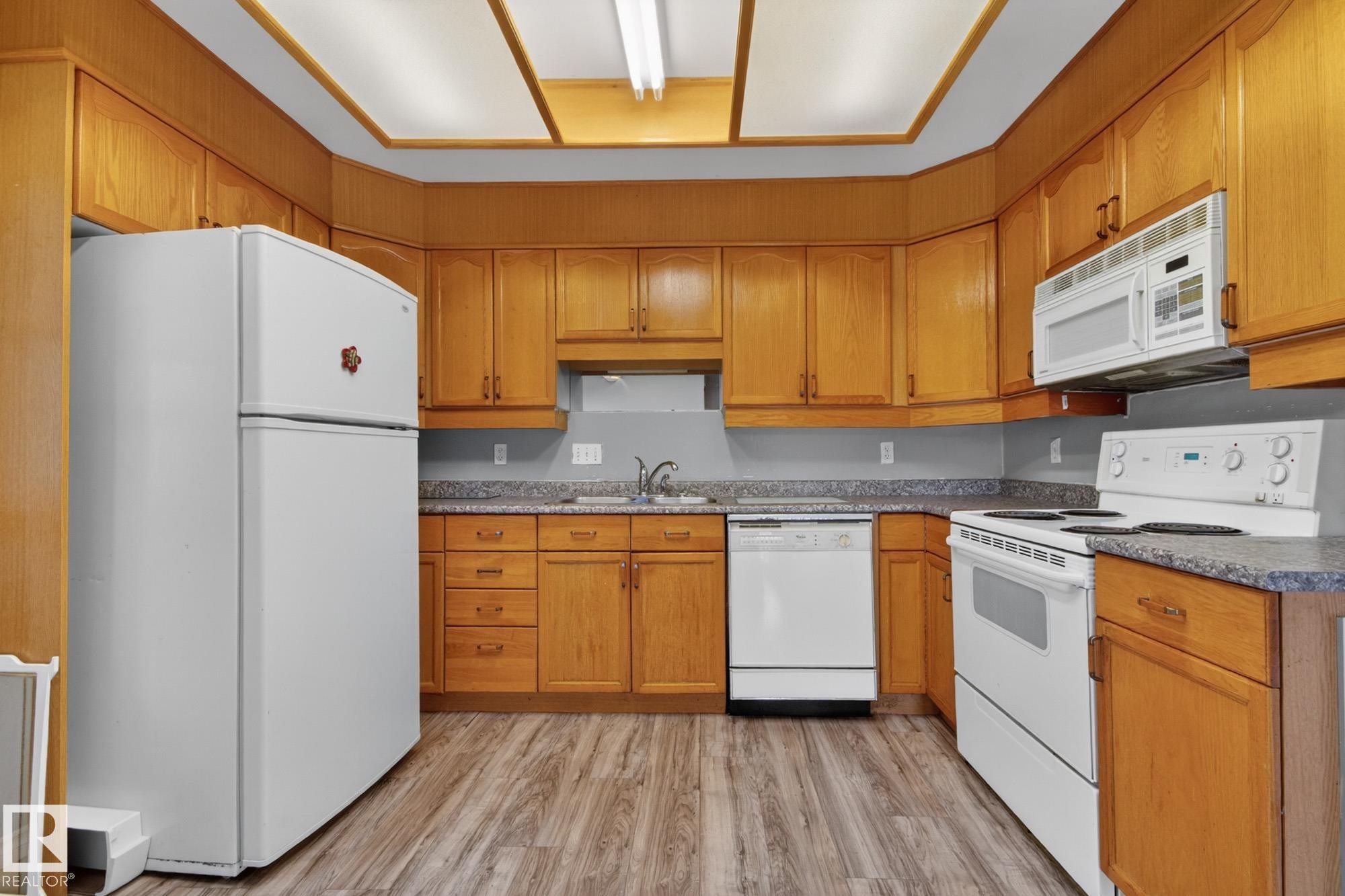 Kitchen featuring wood-finish cabinetry, speckled countertops, and wood-finish flooring - 11901 42 Street Nw, Edmonton, AB - Indoor Photo Showing Kitchen With Double Sink