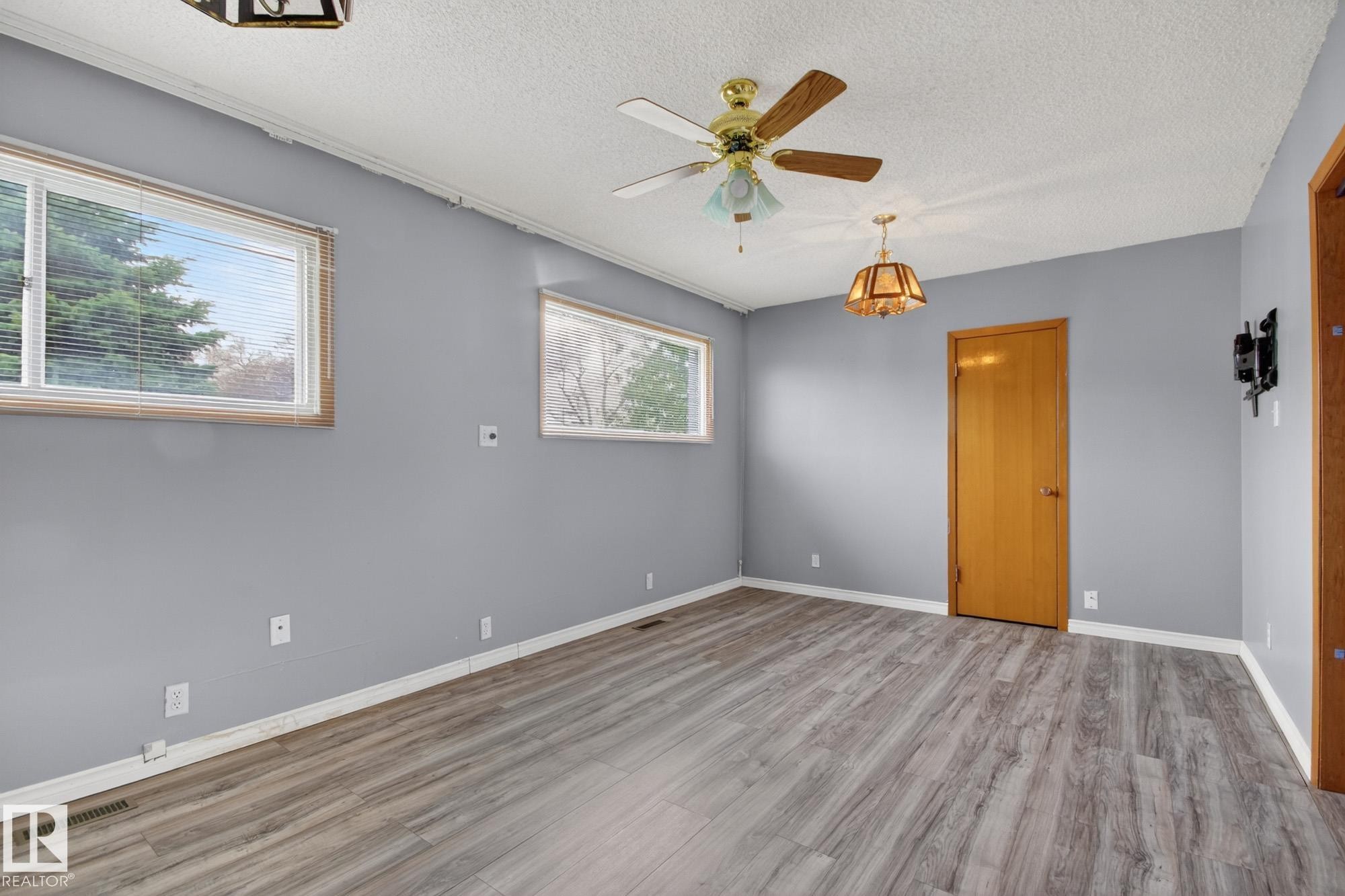 Spacious room featuring wood-finish flooring, light gray wall paint, and two distinct overhead light fixtures - 11901 42 Street Nw, Edmonton, AB - Indoor Photo Showing Other Room