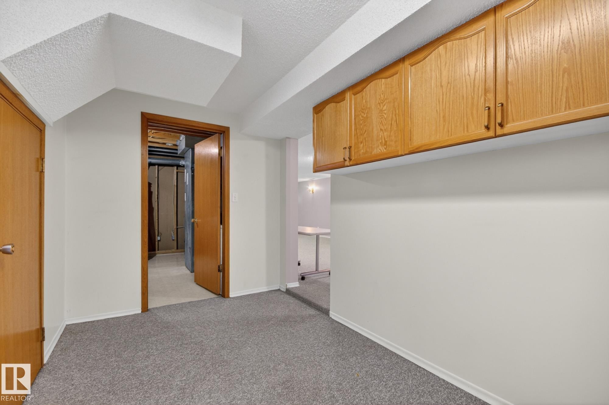 Carpeted room featuring light gray walls, built-in wood-finish cabinetry, and a solid wood interior door - 11901 42 Street Nw, Edmonton, AB - Indoor Photo Showing Other Room
