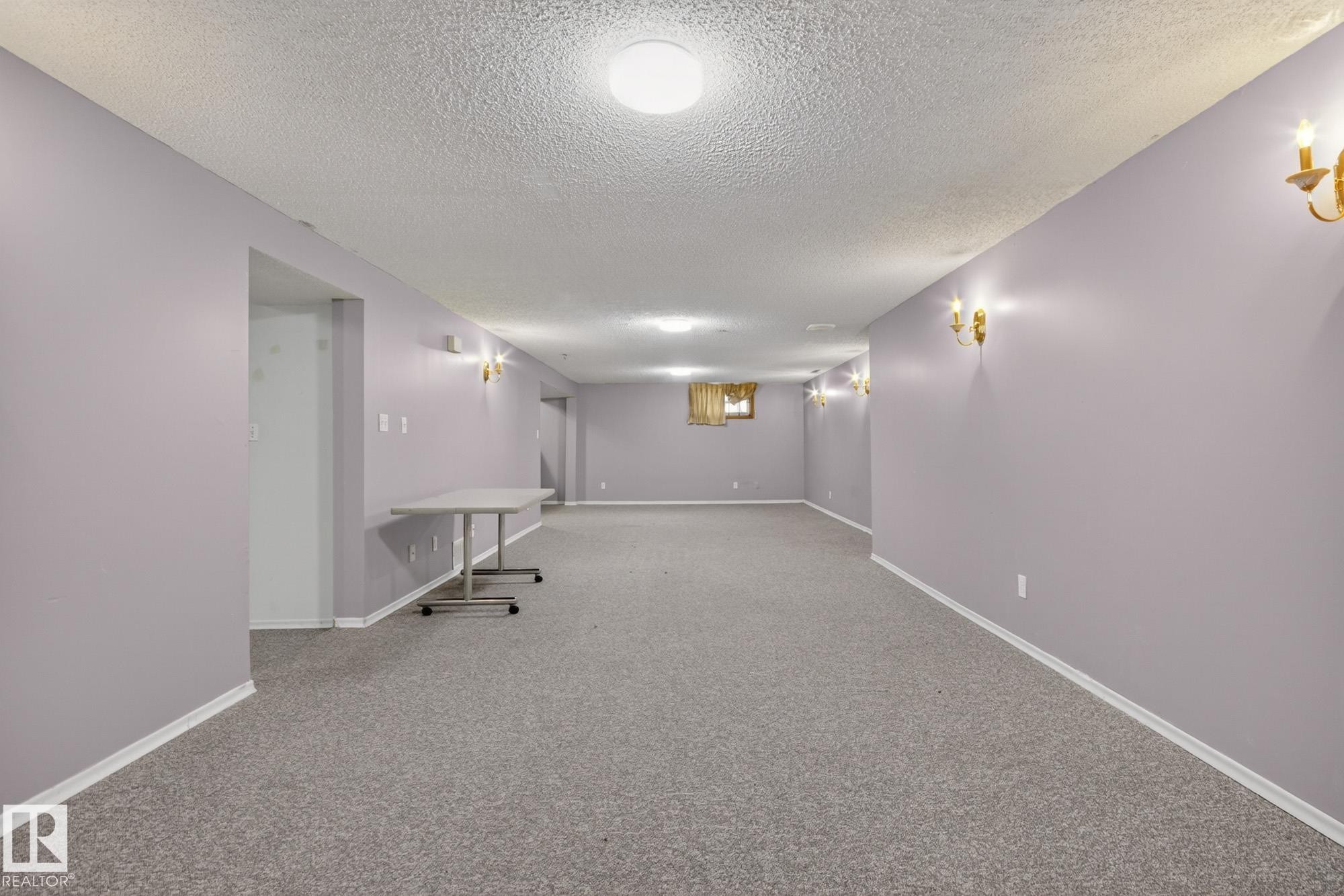 Spacious room featuring light lavender walls, gray carpet flooring, white baseboards, and multiple gold-toned wall sconces - 11901 42 Street Nw, Edmonton, AB - Indoor Photo Showing Other Room