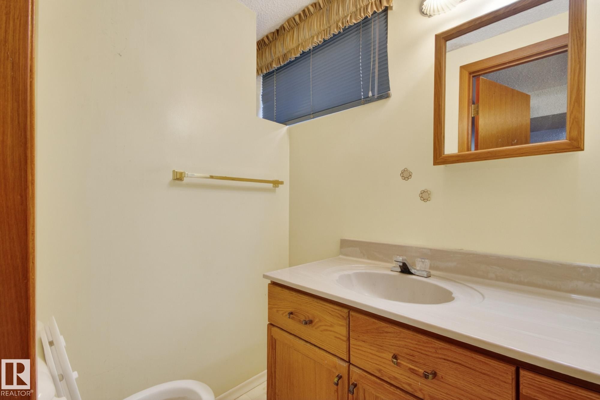 Bathroom vanity with an integrated sink, wood-finish cabinetry, and a framed mirror - 11901 42 Street Nw, Edmonton, AB - Indoor Photo Showing Bathroom