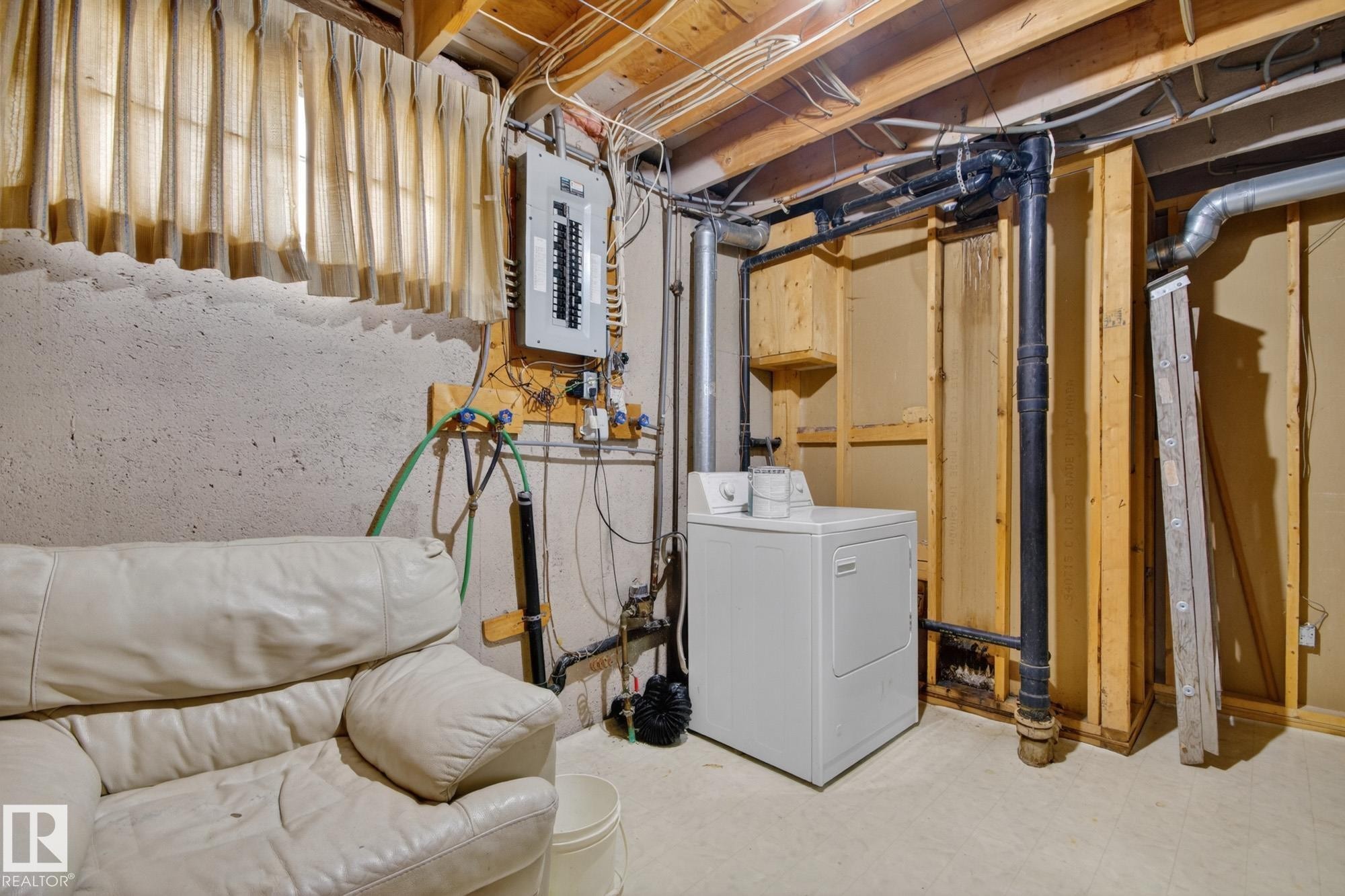 Utility area featuring exposed ceiling joists, electrical panel, cement flooring, and a window with light-filtering curtains - 11901 42 Street Nw, Edmonton, AB - Indoor Photo Showing Laundry Room