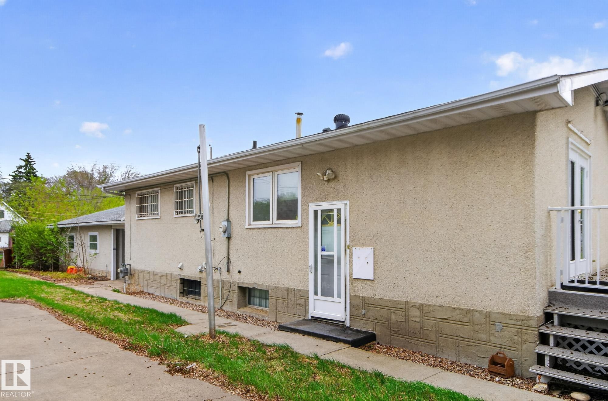 Stucco exterior featuring multiple entry points and exposed aggregate foundation detailing - 11901 42 Street Nw, Edmonton, AB - Outdoor With Exterior