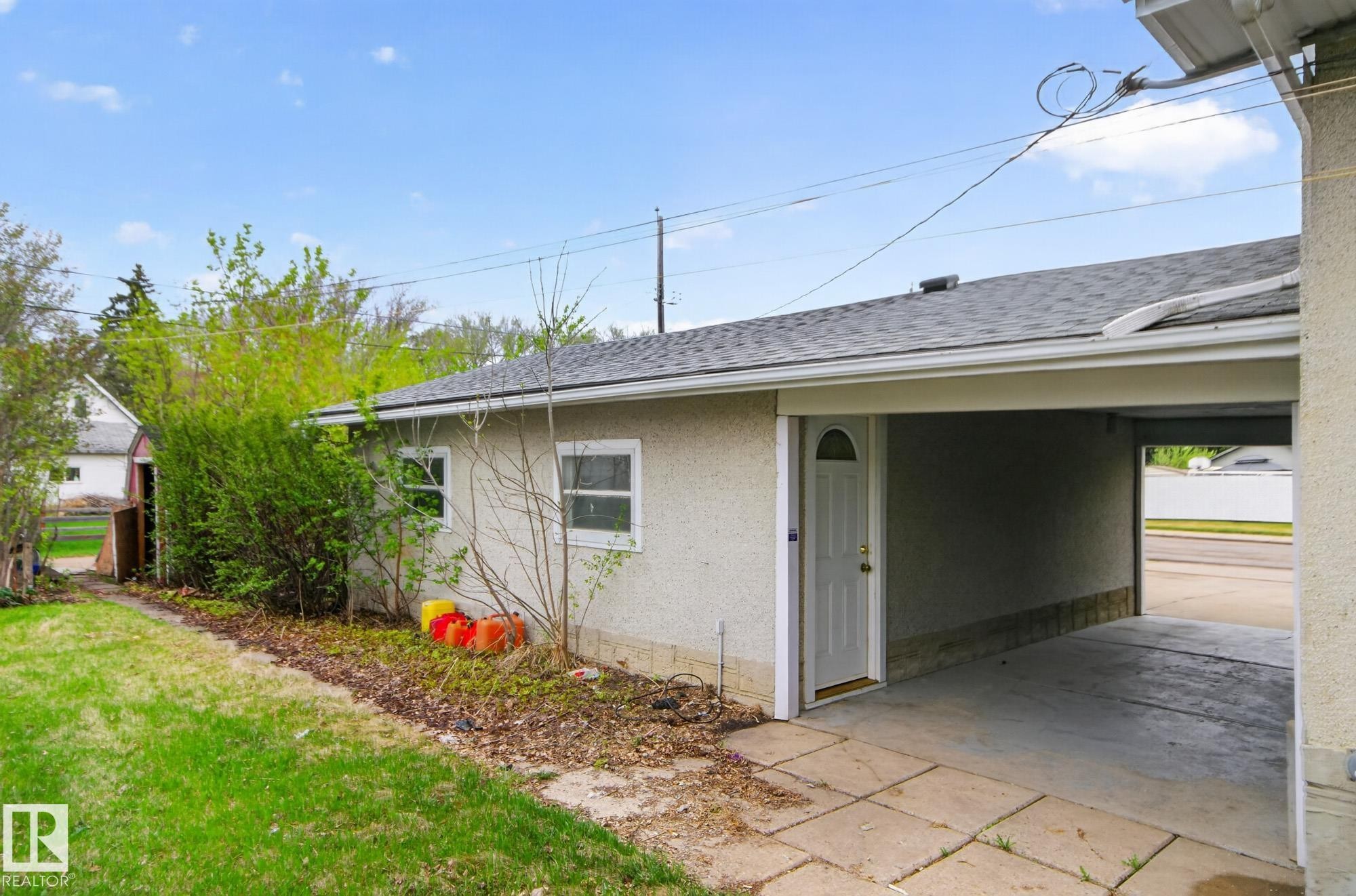 Exterior stucco finish building with a carport featuring a concrete floor and a side entry door with an arched window - 11901 42 Street Nw, Edmonton, AB - Outdoor With Exterior