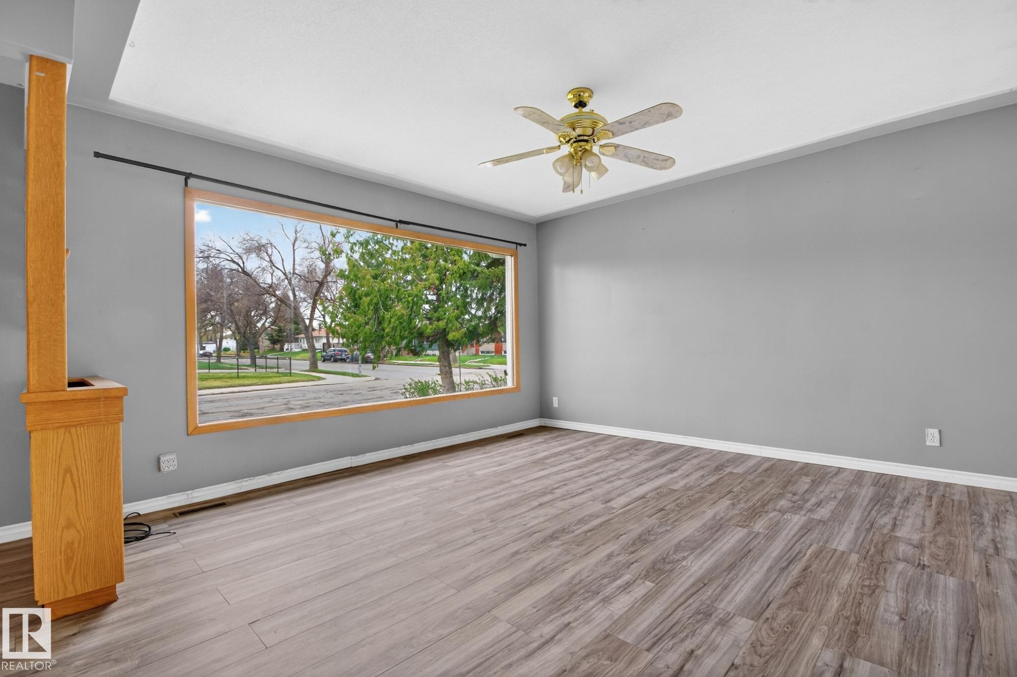 Spacious room featuring wood-finish flooring, a large picture window with natural wood trim, and a ceiling fan with light fixture - 11901 42 Street Nw, Edmonton, AB - Indoor Photo Showing Other Room