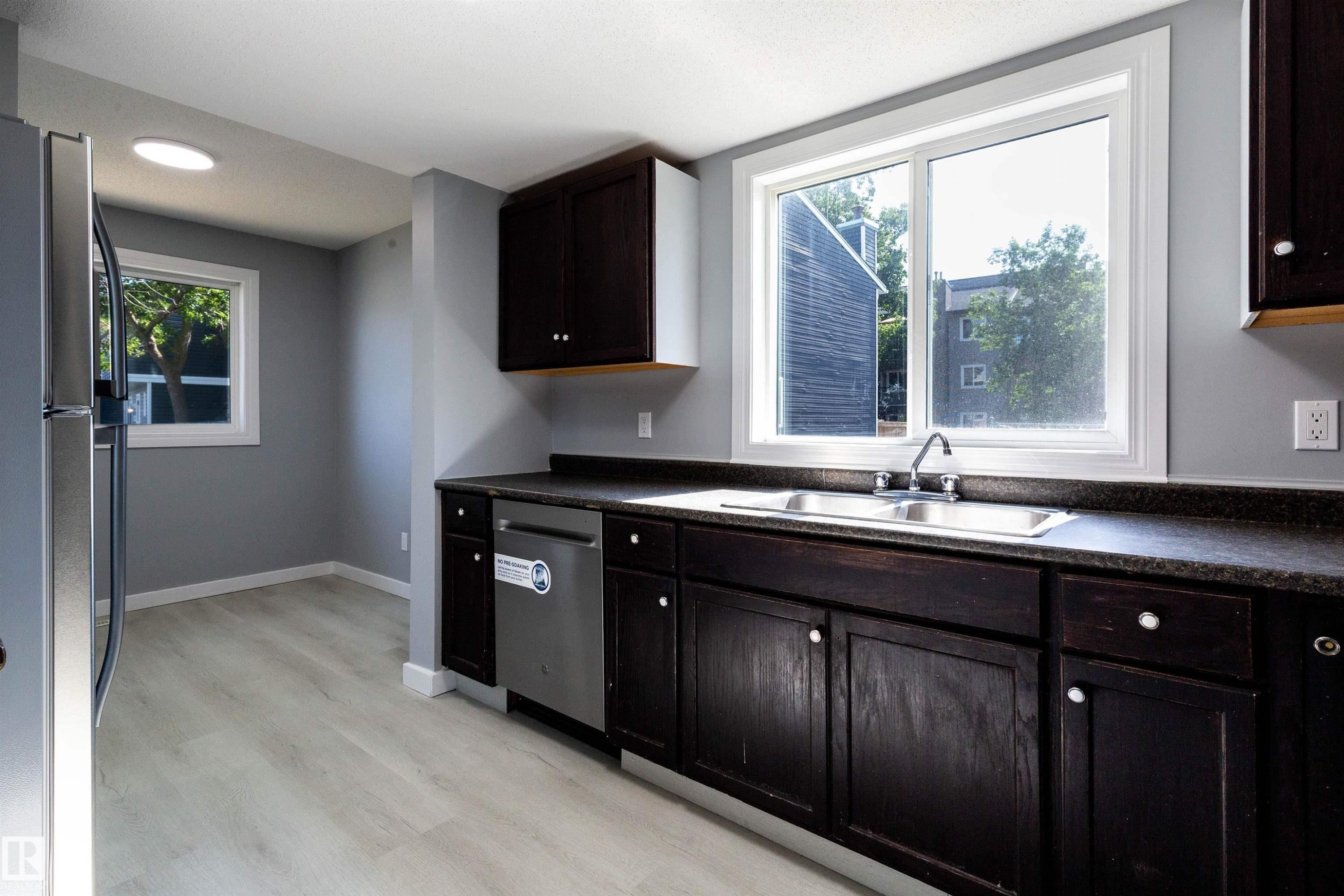 Kitchen featuring dark wood cabinetry, a double basin stainless steel sink, and light wood-finish flooring - 547 Dunluce Road, Edmonton, AB - Indoor Photo Showing Kitchen With Double Sink