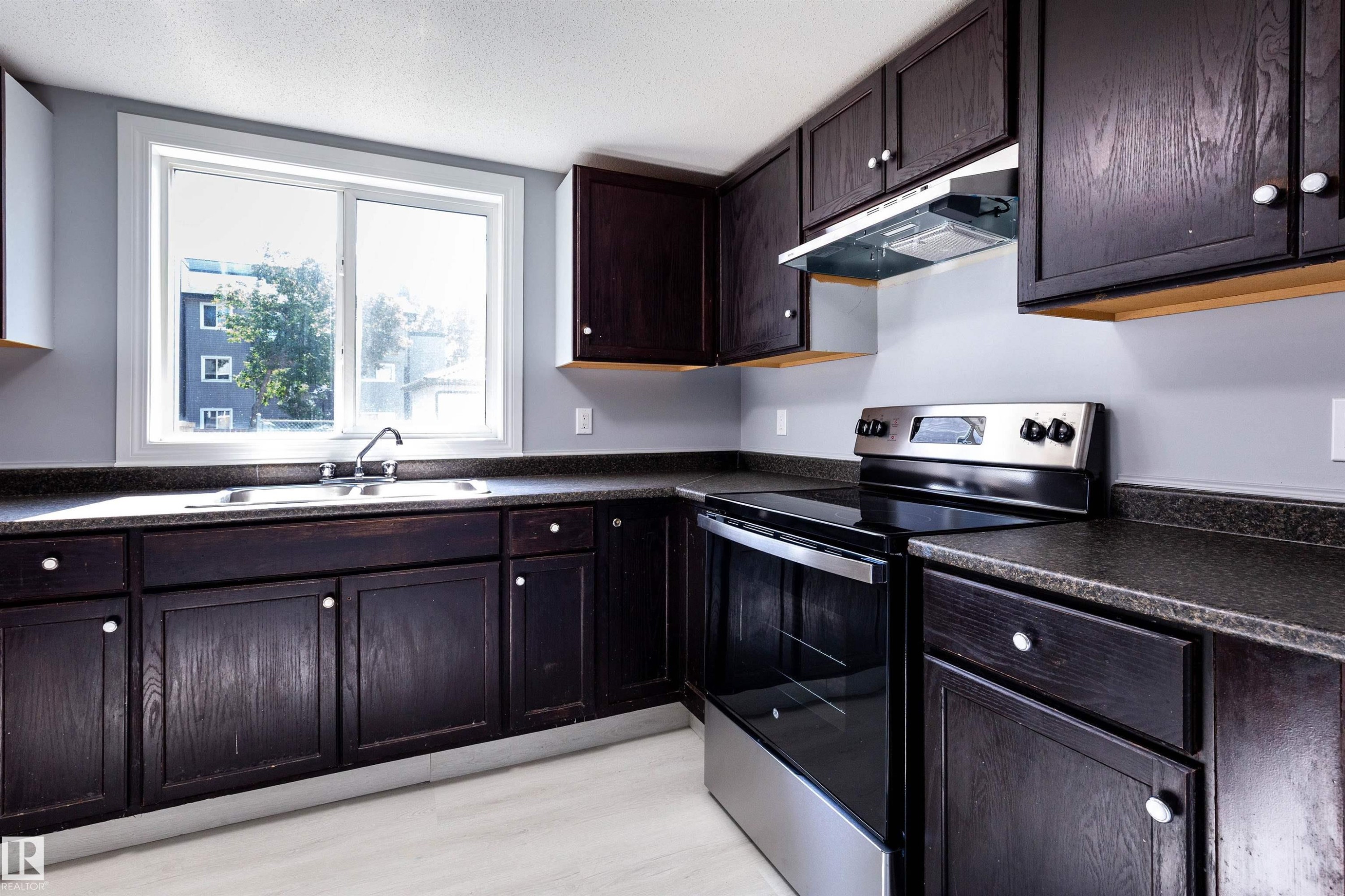 Kitchen featuring dark wood-finish cabinetry, a stainless steel range with overhead hood, and a dual basin sink beneath a large window - 547 Dunluce Road, Edmonton, AB - Indoor Photo Showing Kitchen With Double Sink