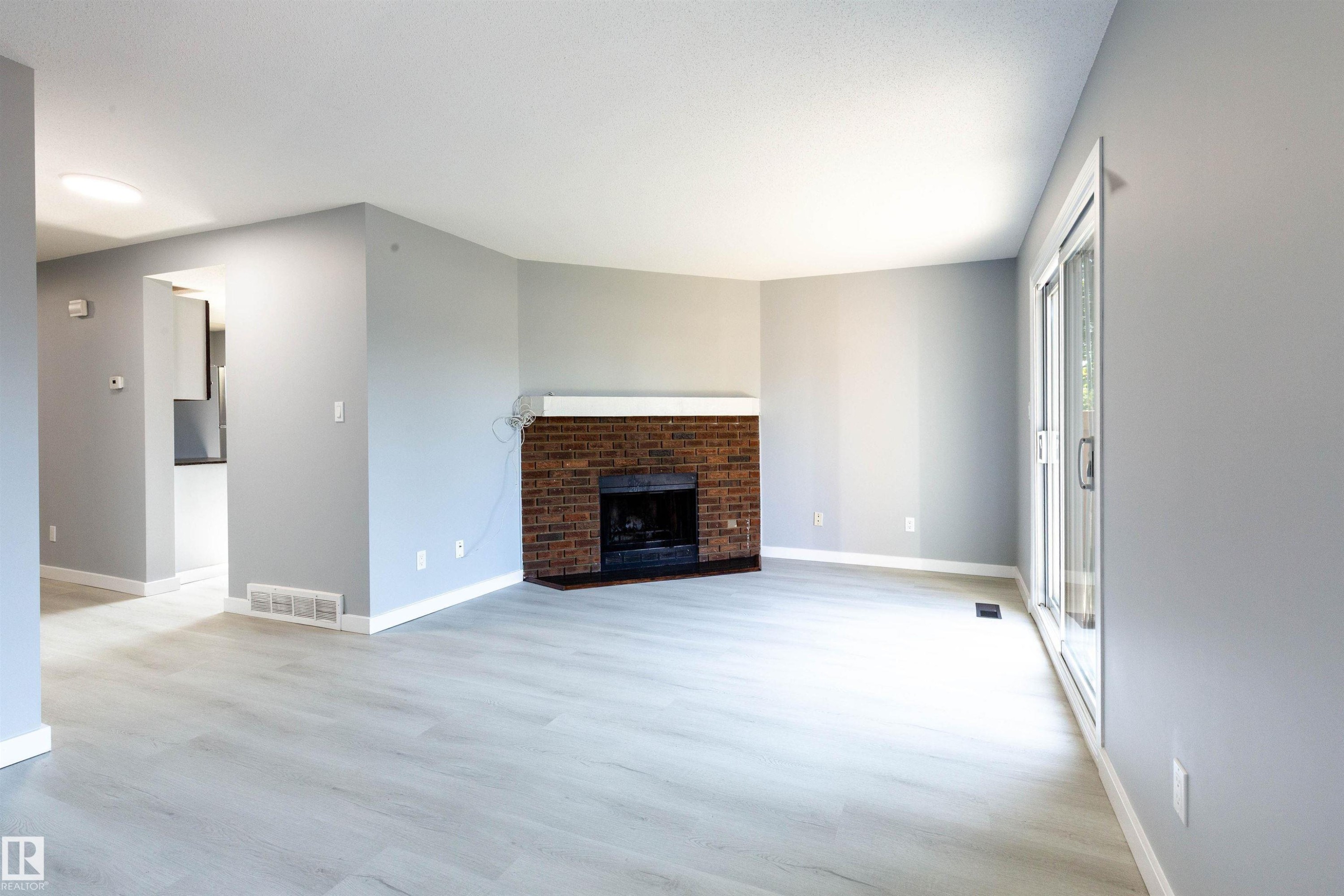 Living room featuring a brick fireplace with a white mantle, light wood-finish flooring, and a sliding glass door - 547 Dunluce Road, Edmonton, AB - Indoor Photo Showing Living Room With Fireplace