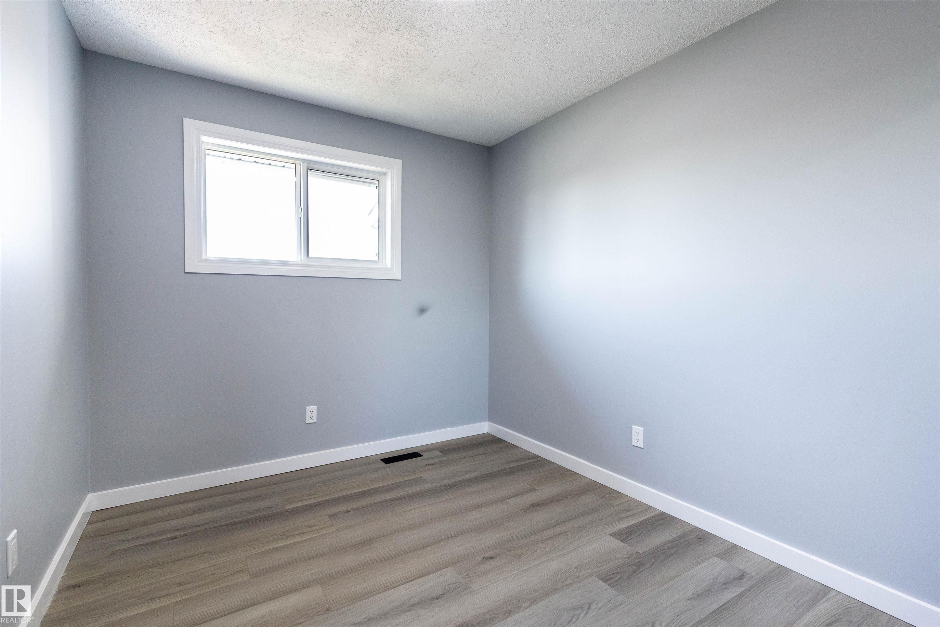 Room featuring neutral gray walls, a white-framed window, textured ceiling, light wood-finish flooring, and white baseboards - 547 Dunluce Road, Edmonton, AB - Indoor Photo Showing Other Room