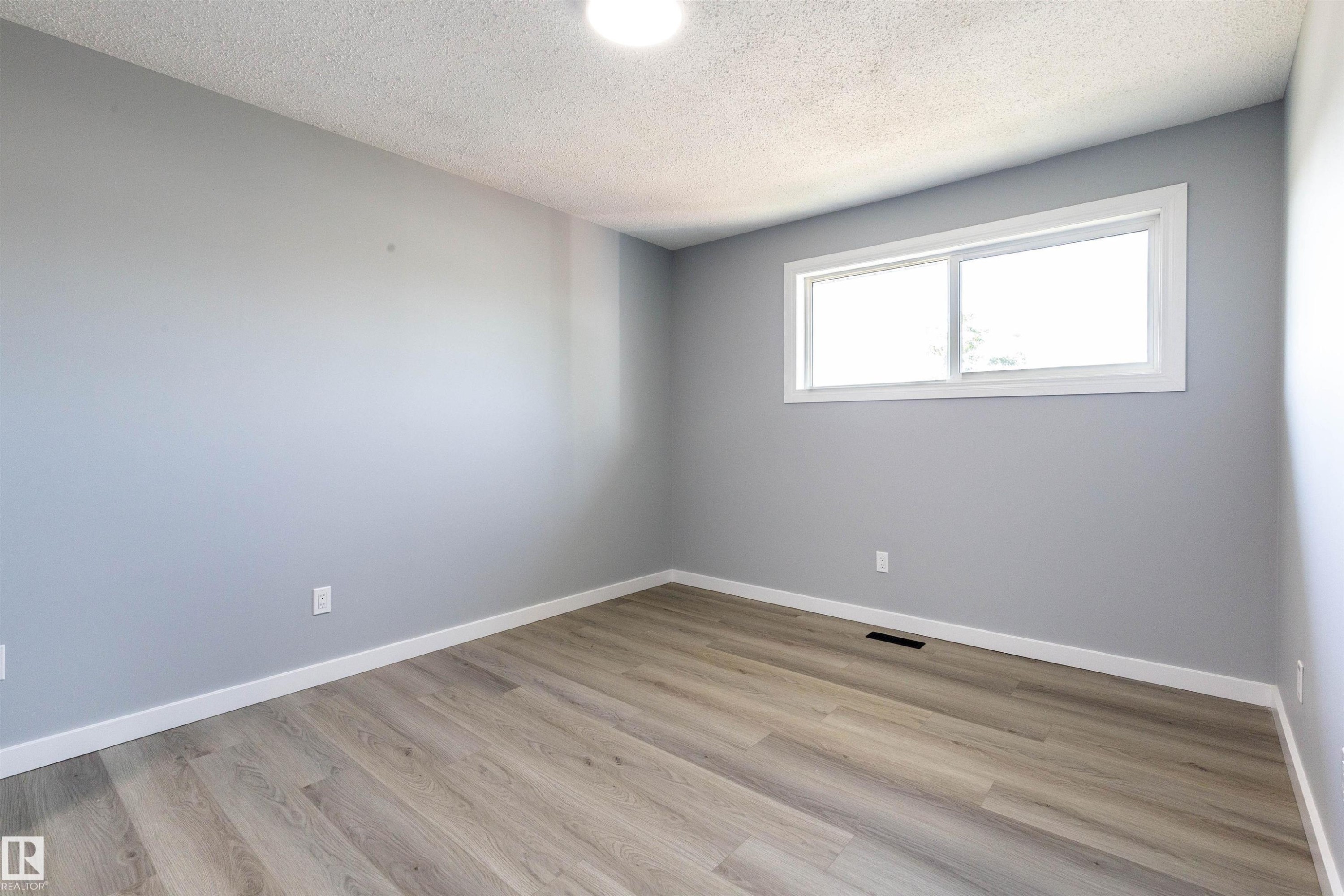 Room featuring a large window, light gray walls, wood-finish flooring, white baseboards, and a ceiling-mounted light fixture - 547 Dunluce Road, Edmonton, AB - Indoor Photo Showing Other Room