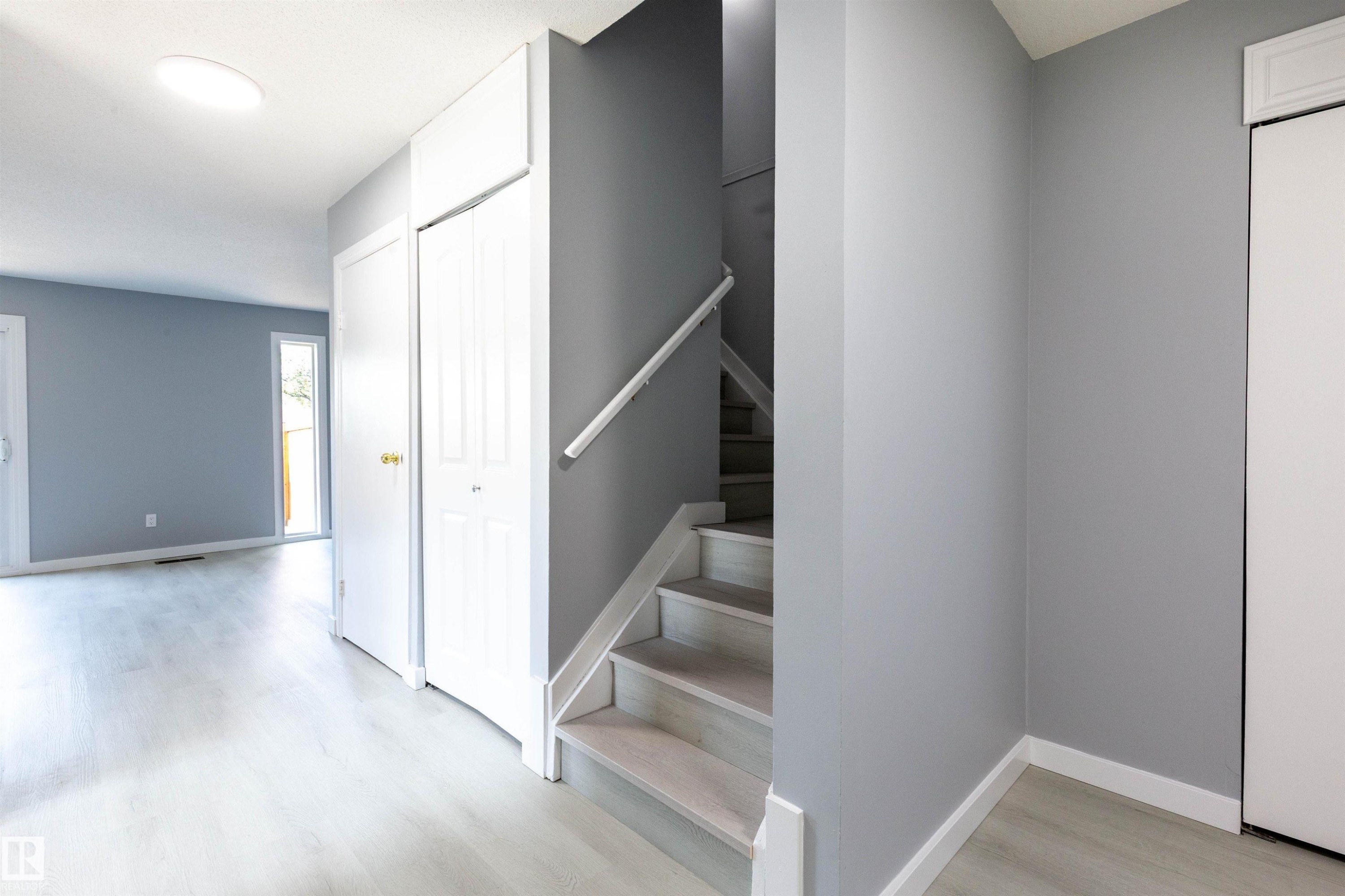 Entryway featuring wood-finish flooring, a contemporary ceiling light fixture, a staircase with a light-toned handrail, and white bi-fold closet doors - 547 Dunluce Road, Edmonton, AB - Indoor Photo Showing Other Room