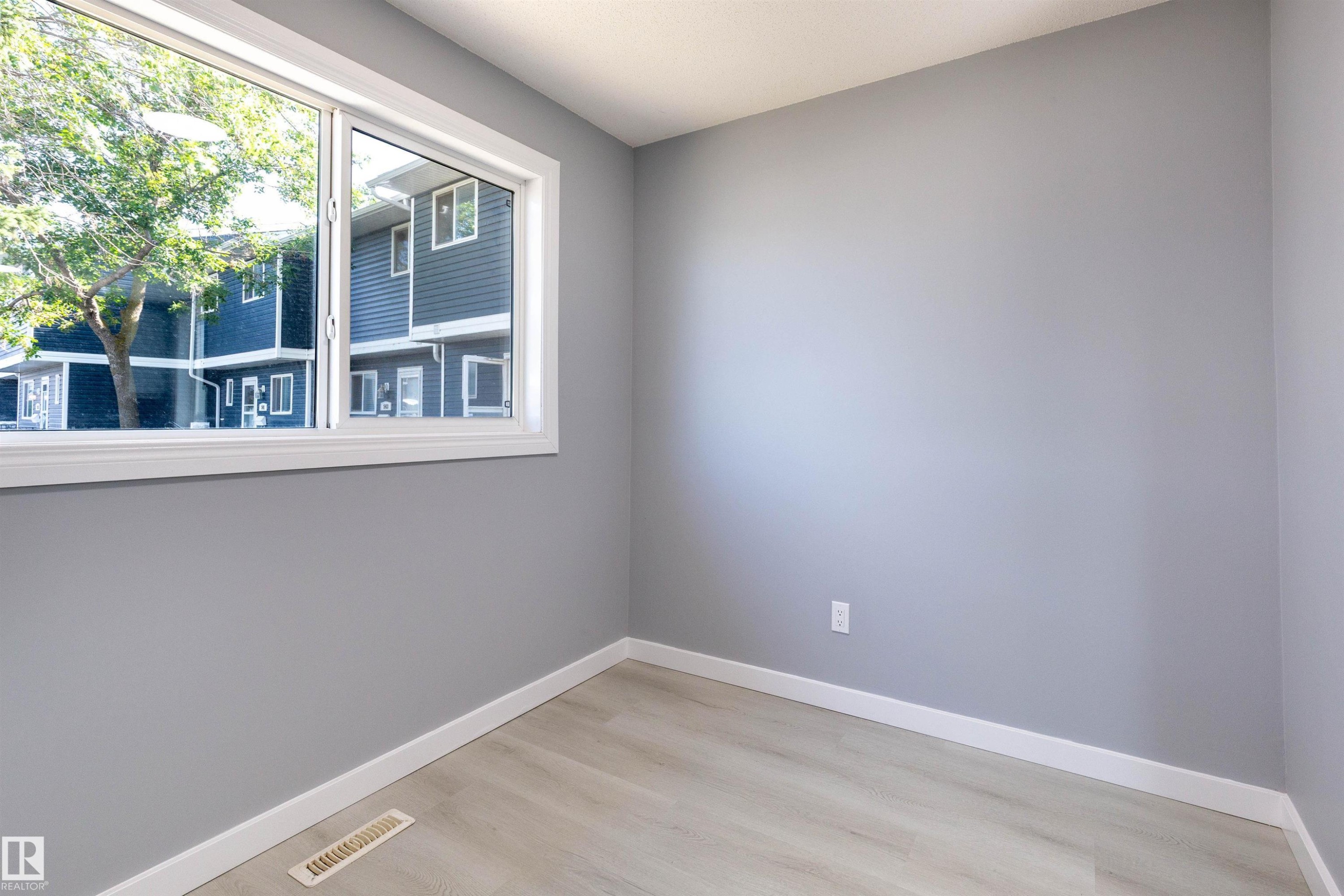 Bright interior space featuring a large window with white trim, light-toned wood-finish flooring, gray walls, and white baseboards - 547 Dunluce Road, Edmonton, AB - Indoor Photo Showing Other Room