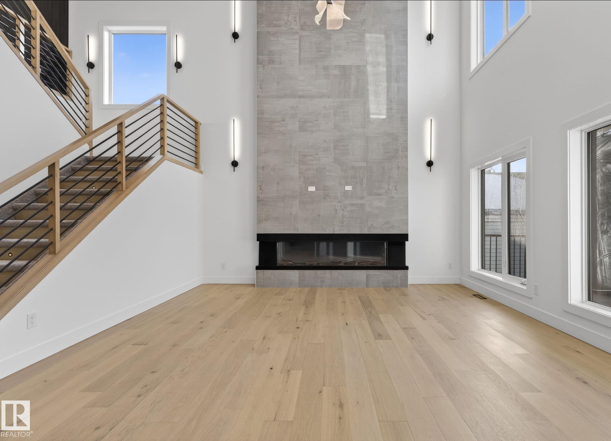 Two-story living area featuring a full-height tiled fireplace, light wood-finish flooring, a contemporary wood and metal railing staircase, and large windows - 5820 110 Street, Edmonton, AB - Indoor With Fireplace
