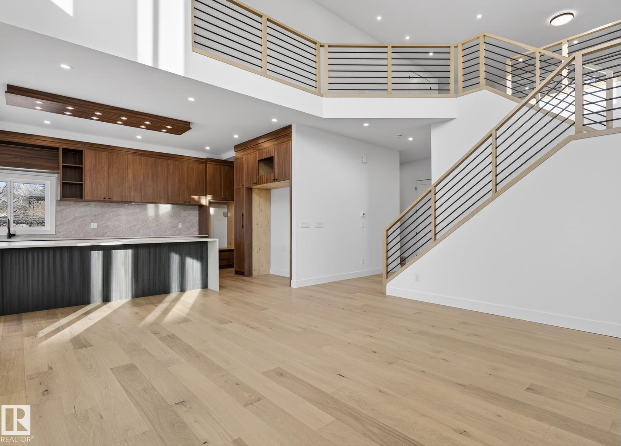 Open-concept living area featuring light wood-finish flooring, a two-story ceiling, and a contemporary staircase with wood and metal railings - 5820 110 Street, Edmonton, AB - Indoor Photo Showing Kitchen