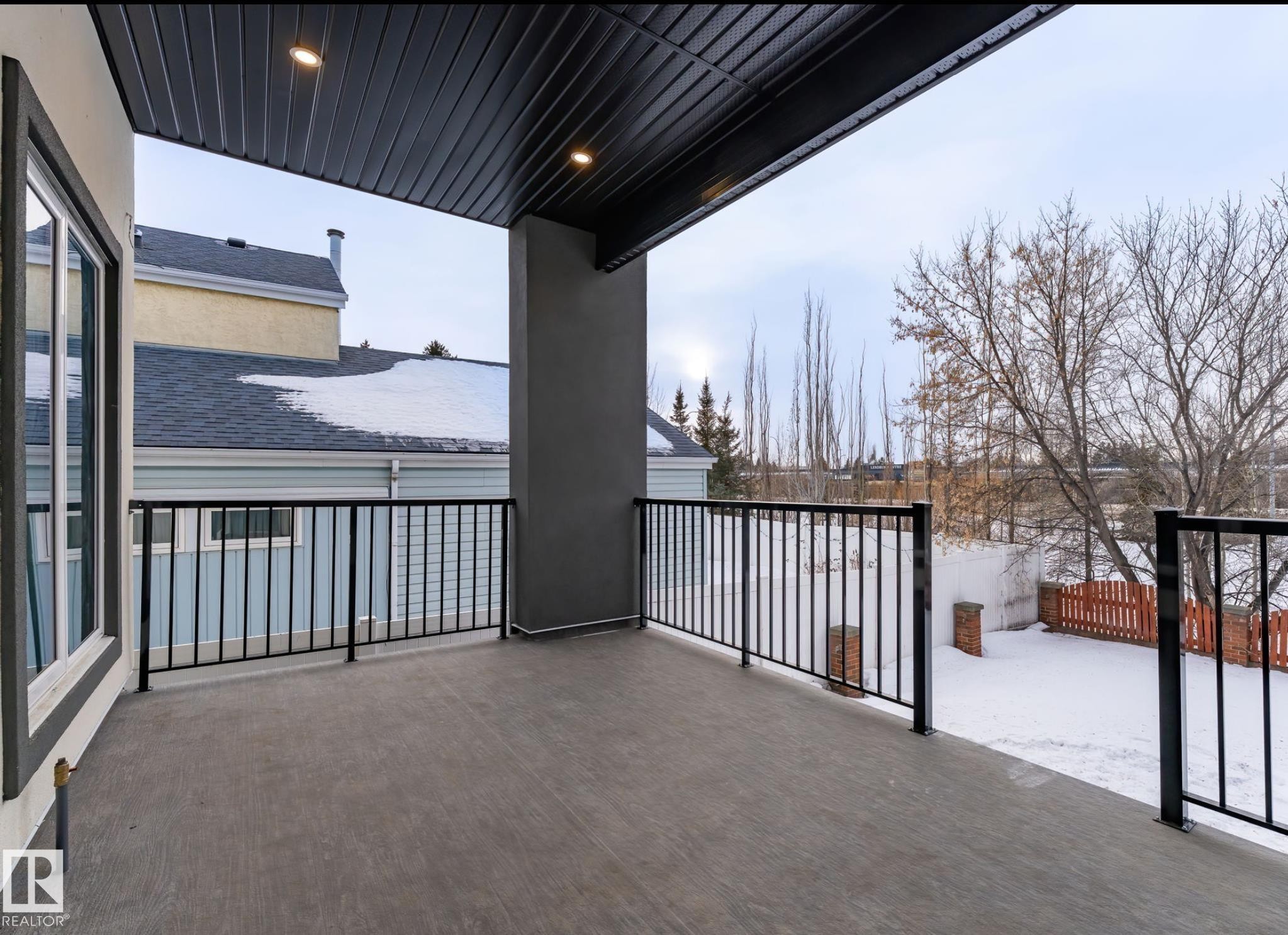 Covered outdoor patio featuring a textured concrete surface, black metal railings, and integrated overhead lighting - 5820 110 Street, Edmonton, AB - Outdoor With Balcony With Exterior