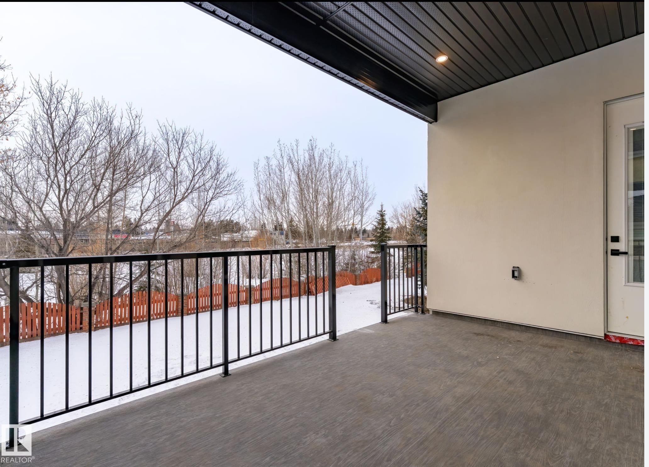 Covered outdoor patio area featuring a textured concrete surface and black metal railings - 5820 110 Street, Edmonton, AB - Outdoor With Balcony With Exterior