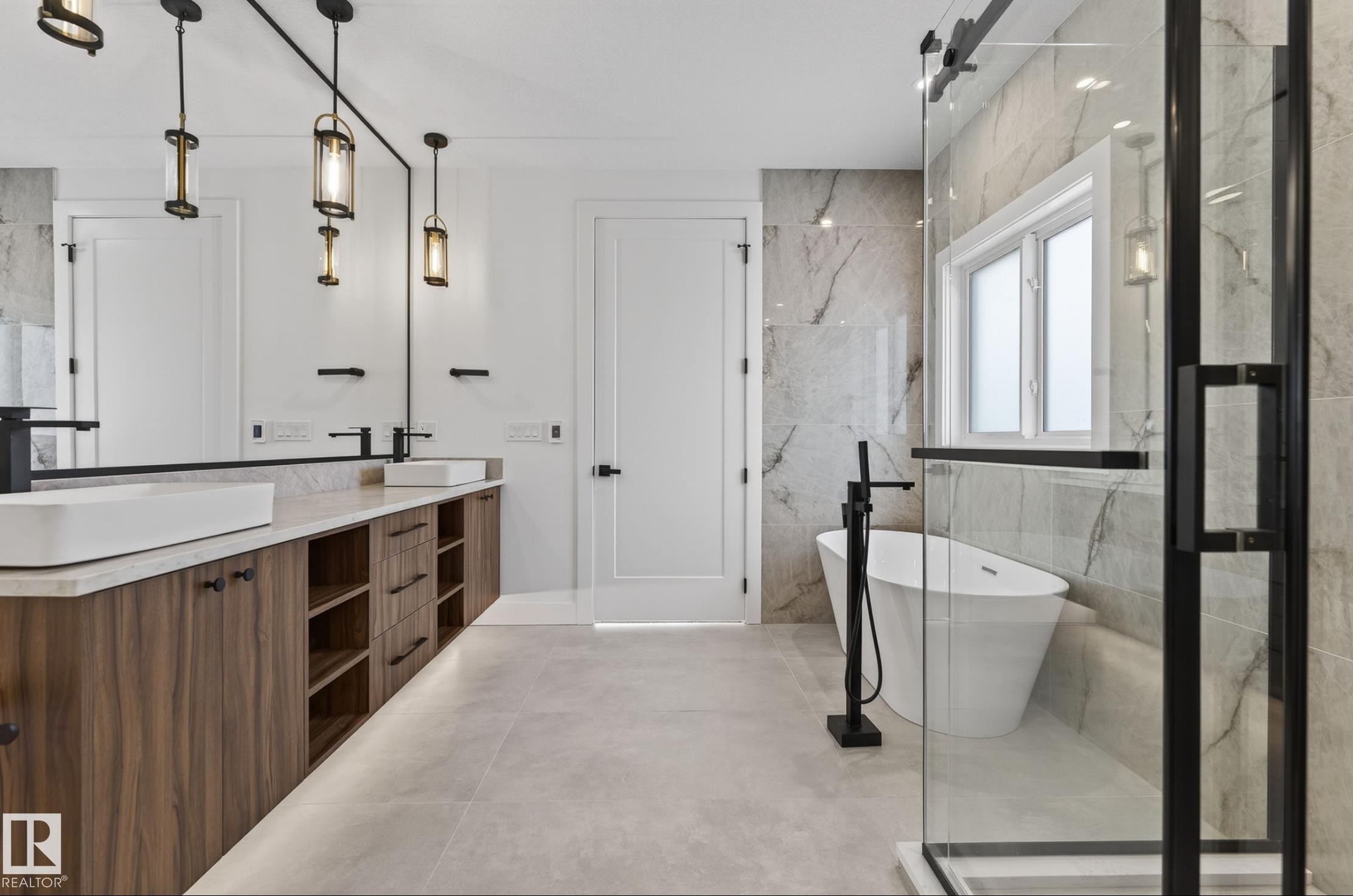 Modern bathroom featuring a freestanding soaking tub with a floor-mounted faucet, a glass-enclosed shower with black trim, and a dual vanity with wood-finish cabinetry, countertop lighting, and vessel sinks - 5820 110 Street, Edmonton, AB - Indoor