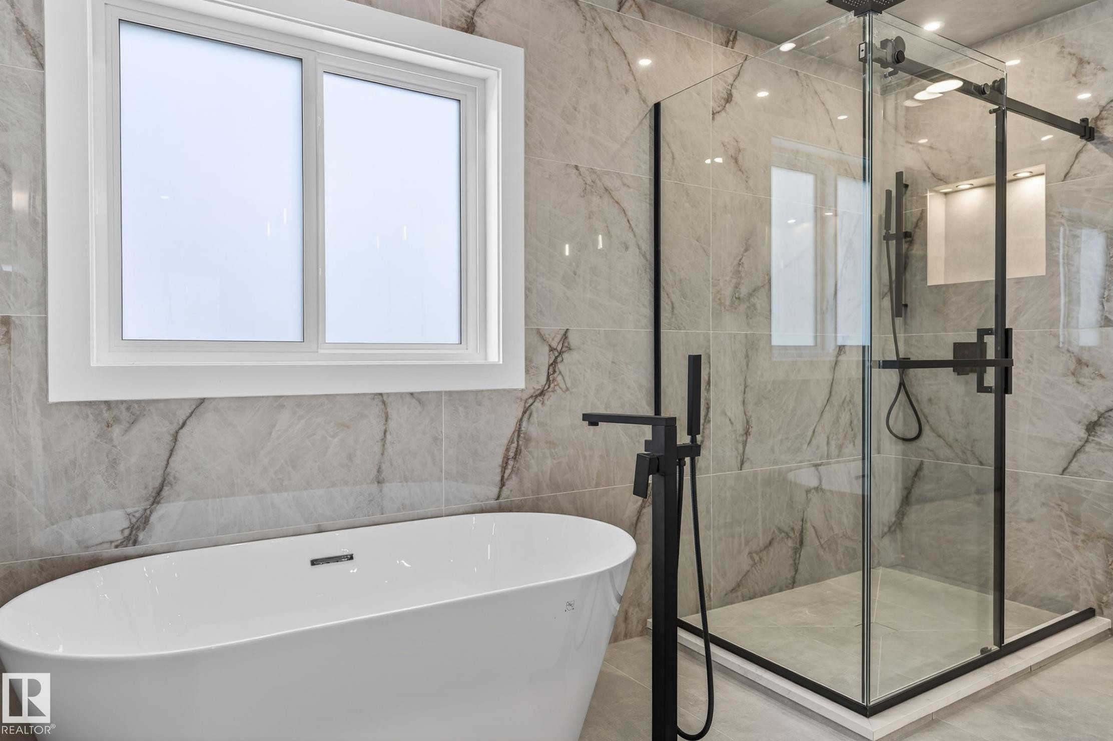 Modern bathroom featuring a freestanding soaking tub with a matte black floor-mounted faucet, a glass-enclosed shower with matte black fixtures, full-height veined tile walls, and a large window with white trim - 5820 110 Street, Edmonton, AB - Indoor Photo Showing Bathroom