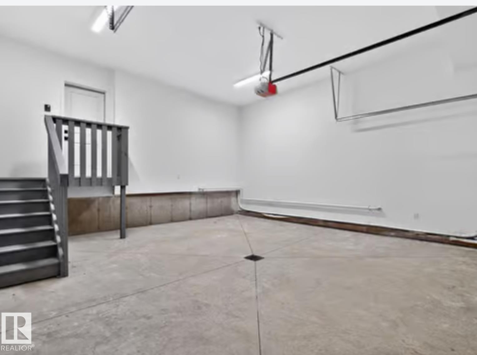 Spacious garage featuring a concrete floor, painted walls, overhead lighting, and a finished staircase with handrails providing interior access - 5820 110 Street, Edmonton, AB - Indoor Photo Showing Other Room