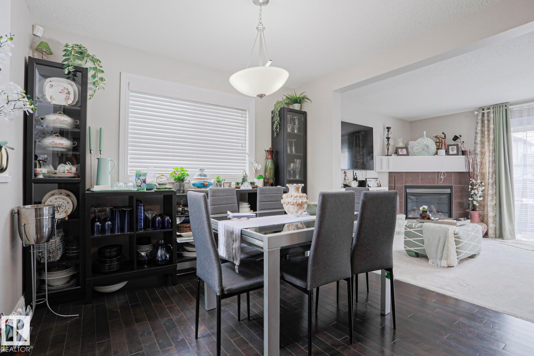 Dining area featuring wood-finish flooring, a contemporary chandelier, and a large window with blinds - 1621 64 Street, Edmonton, AB - Indoor Photo Showing Dining Room With Fireplace