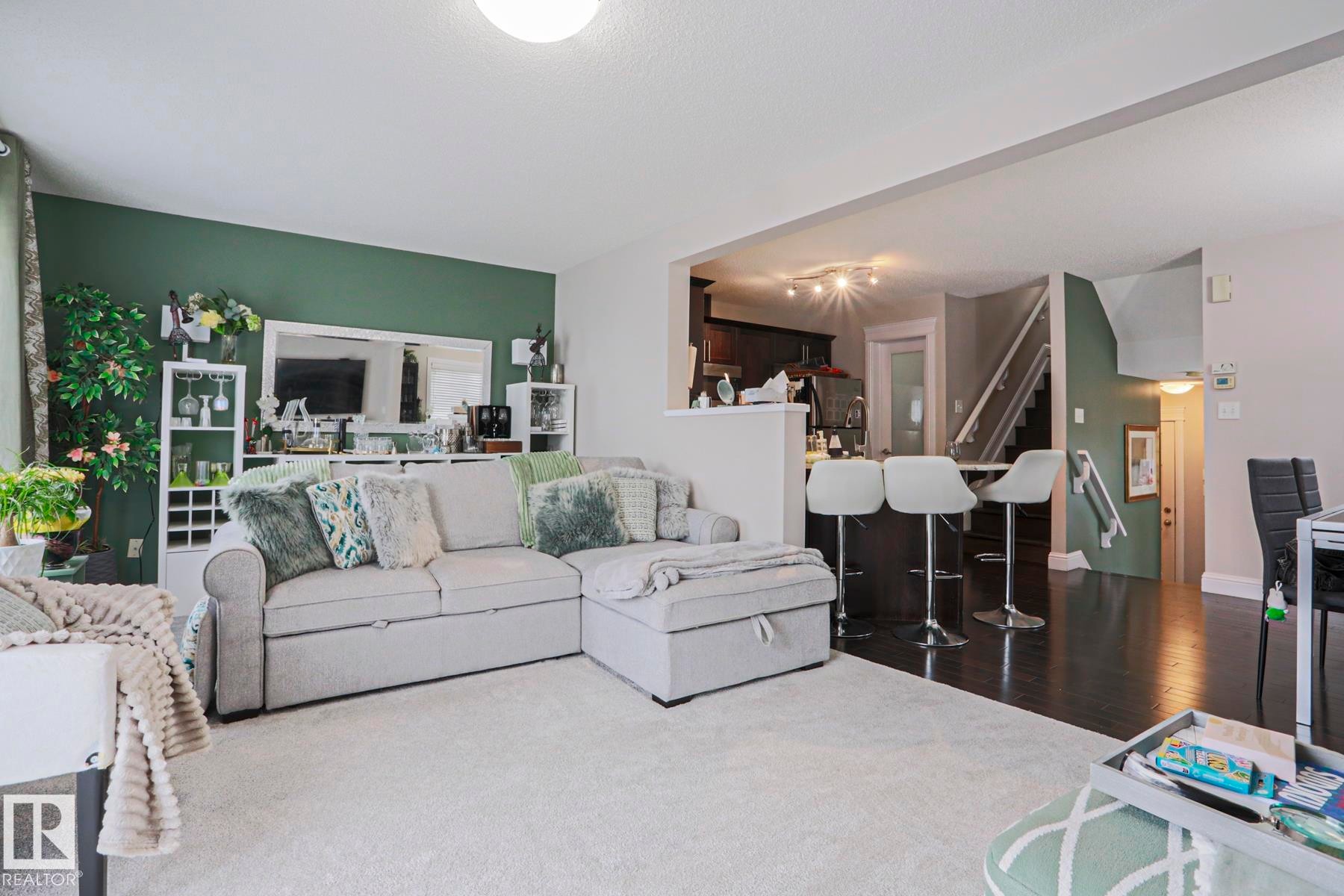Open-concept living area featuring light-toned carpeting, a partial green accent wall, recessed lighting, and an adjacent kitchen space with dark wood-finish flooring and track lighting - 1621 64 Street, Edmonton, AB - Indoor Photo Showing Living Room
