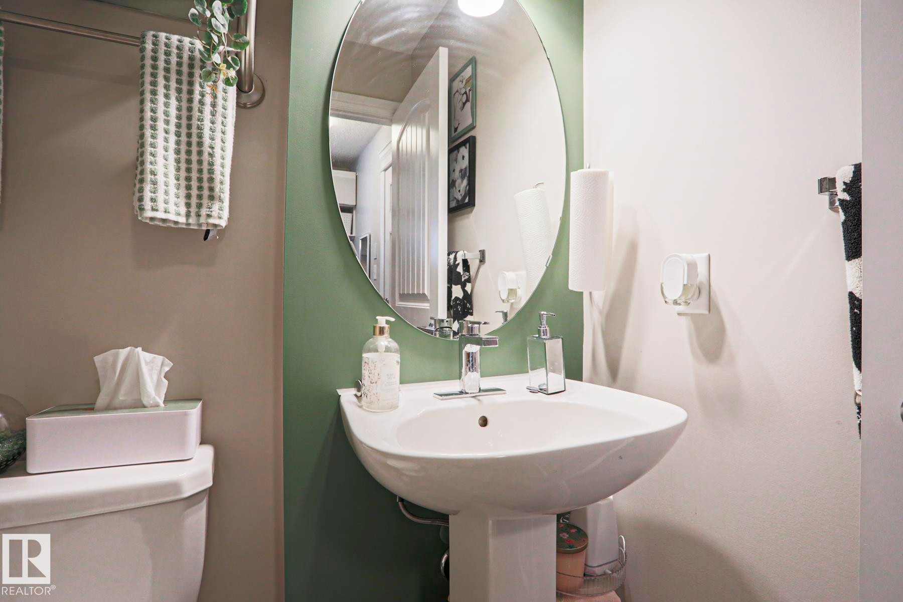 Pedestal sink with chrome faucet, complemented by an oval mirror and two-tone wall finishes - 1621 64 Street, Edmonton, AB - Indoor Photo Showing Bathroom