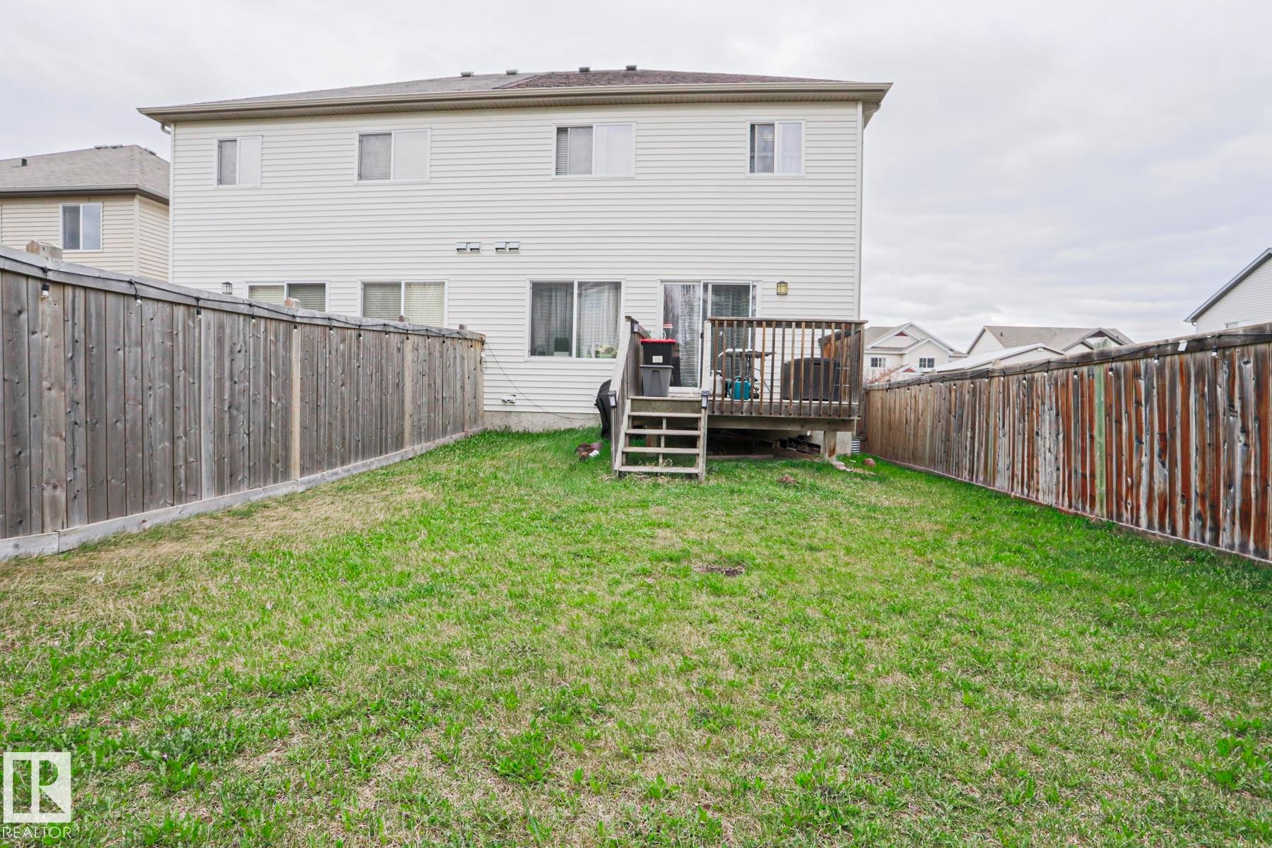 Expansive rear yard featuring a wooden privacy fence, verdant lawn, and a raised wooden deck with stairs to the yard - 1621 64 Street, Edmonton, AB - Outdoor With Deck Patio Veranda With Exterior