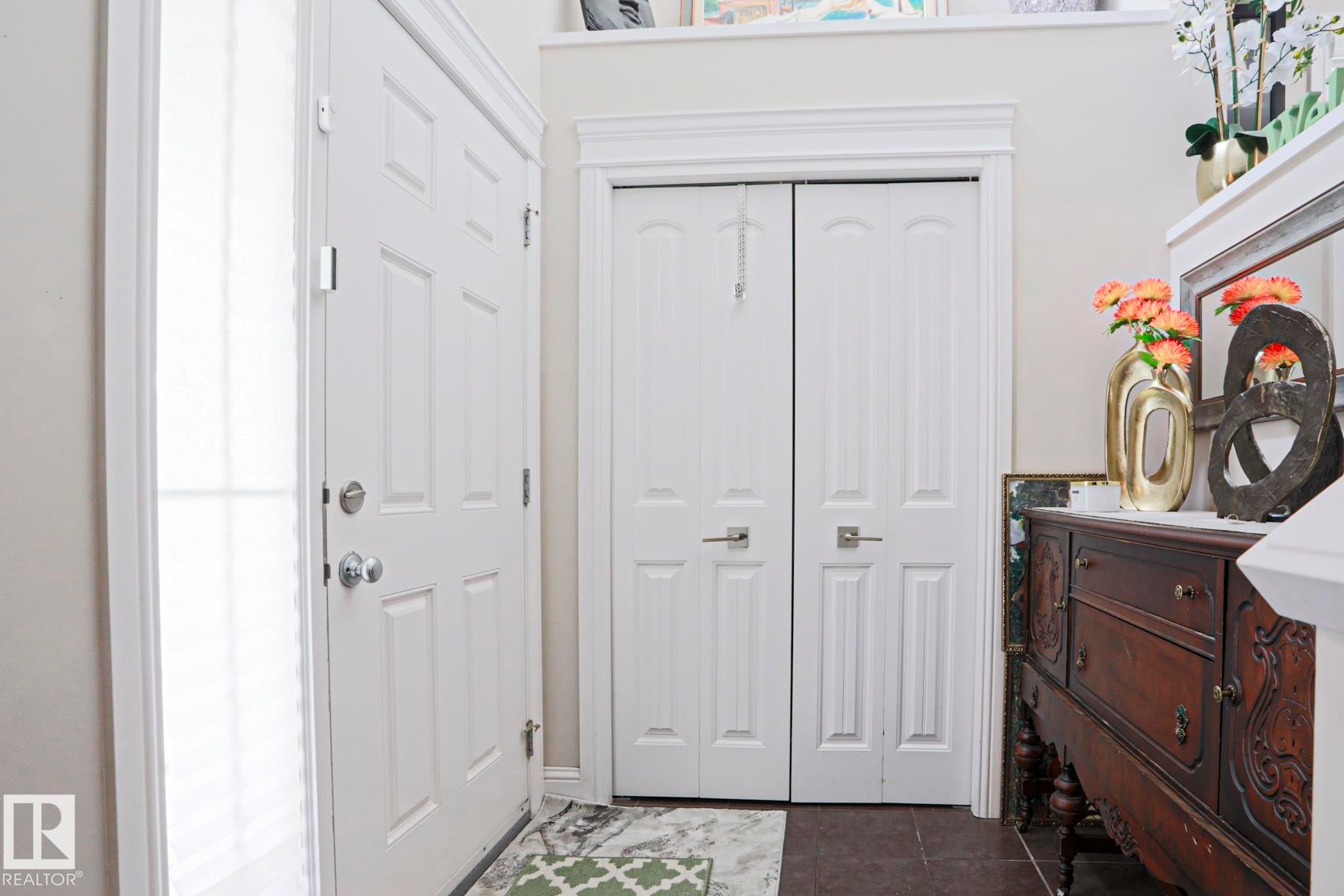 Entryway featuring a white paneled front door with a full-length sidelight, a bi-fold closet with matching hardware, crown molding, and dark tile flooring - 1621 64 Street, Edmonton, AB - Indoor Photo Showing Other Room