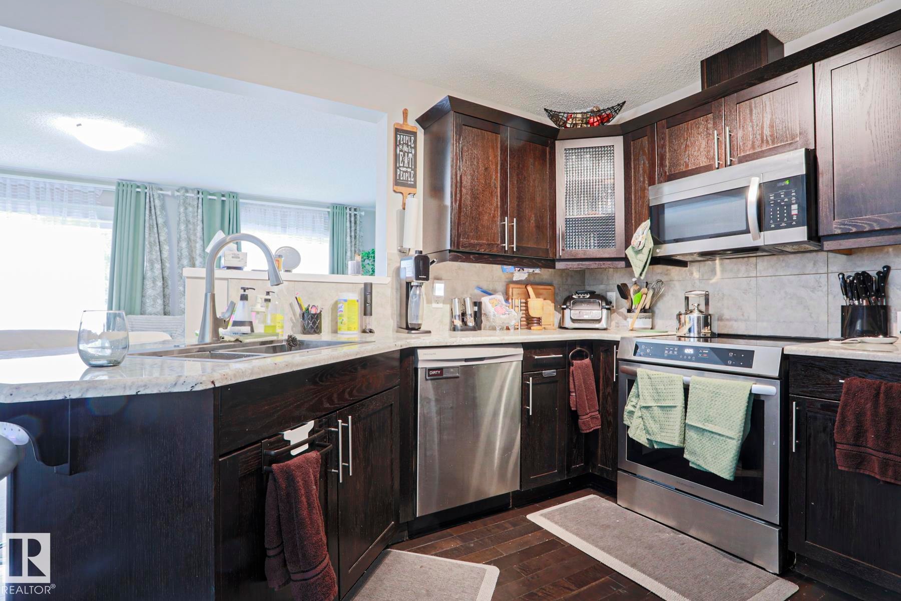 Kitchen featuring dark wood-finish cabinetry, stainless steel appliances, granite countertops, and a tile backsplash - 1621 64 Street, Edmonton, AB - Indoor Photo Showing Kitchen With Double Sink
