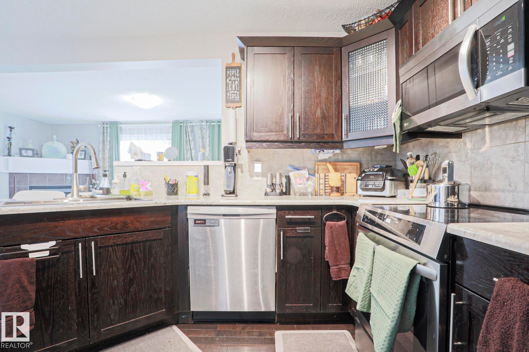 Kitchen featuring dark wood-finish cabinetry, stainless steel appliances, a tile backsplash, and light-toned countertops - 1621 64 Street, Edmonton, AB - Indoor Photo Showing Kitchen With Stainless Steel Kitchen With Double Sink