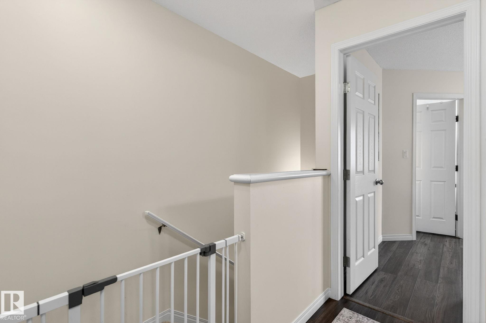 Hallway featuring wood-finish flooring, light-colored walls, white trim, and white paneled doors - 16 7503 Getty Gate, Edmonton, AB - Indoor Photo Showing Other Room