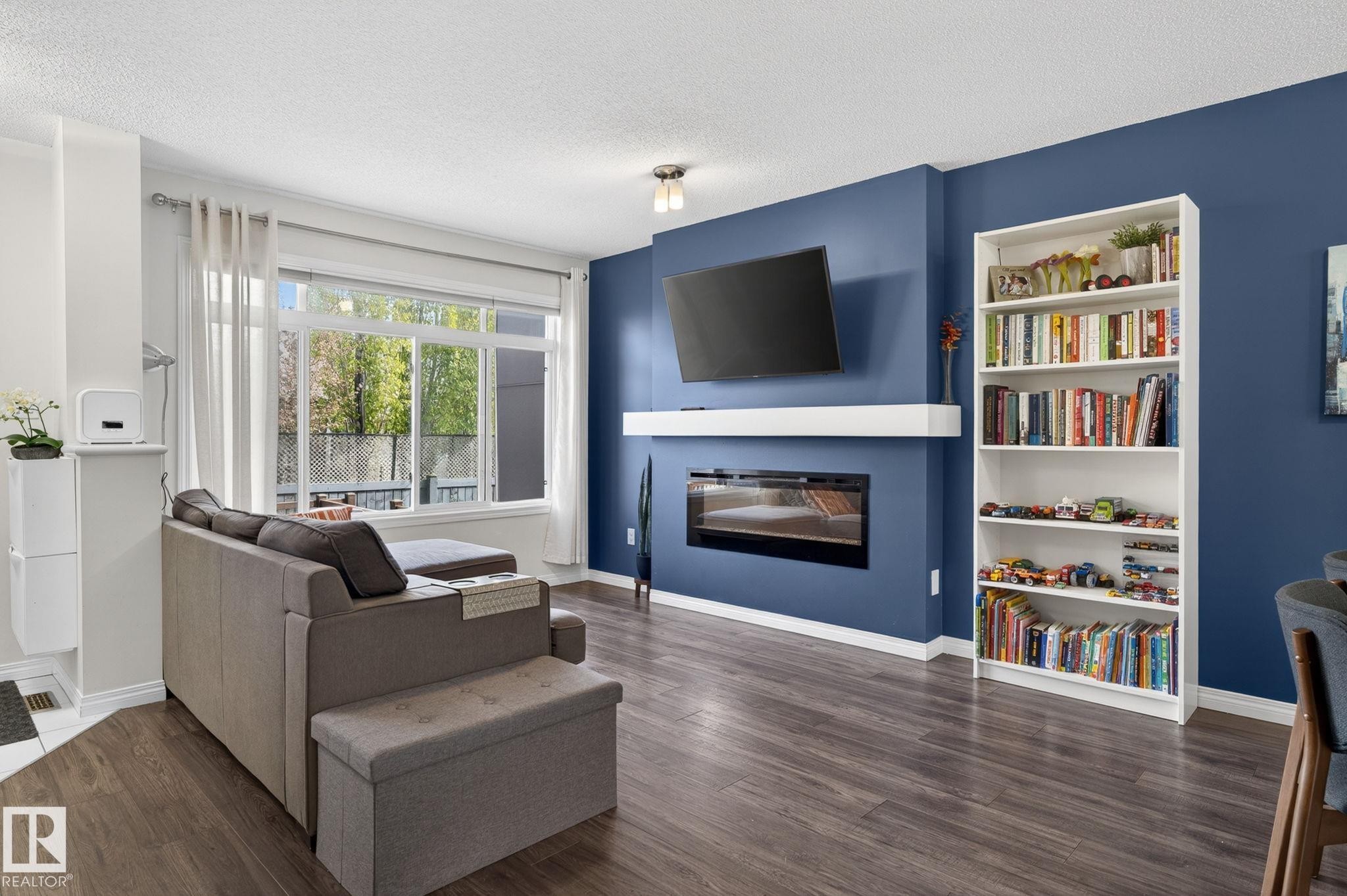 Living area featuring wood-finish flooring and a built-in electric fireplace with a white mantel - 16 7503 Getty Gate, Edmonton, AB - Indoor Photo Showing Living Room With Fireplace