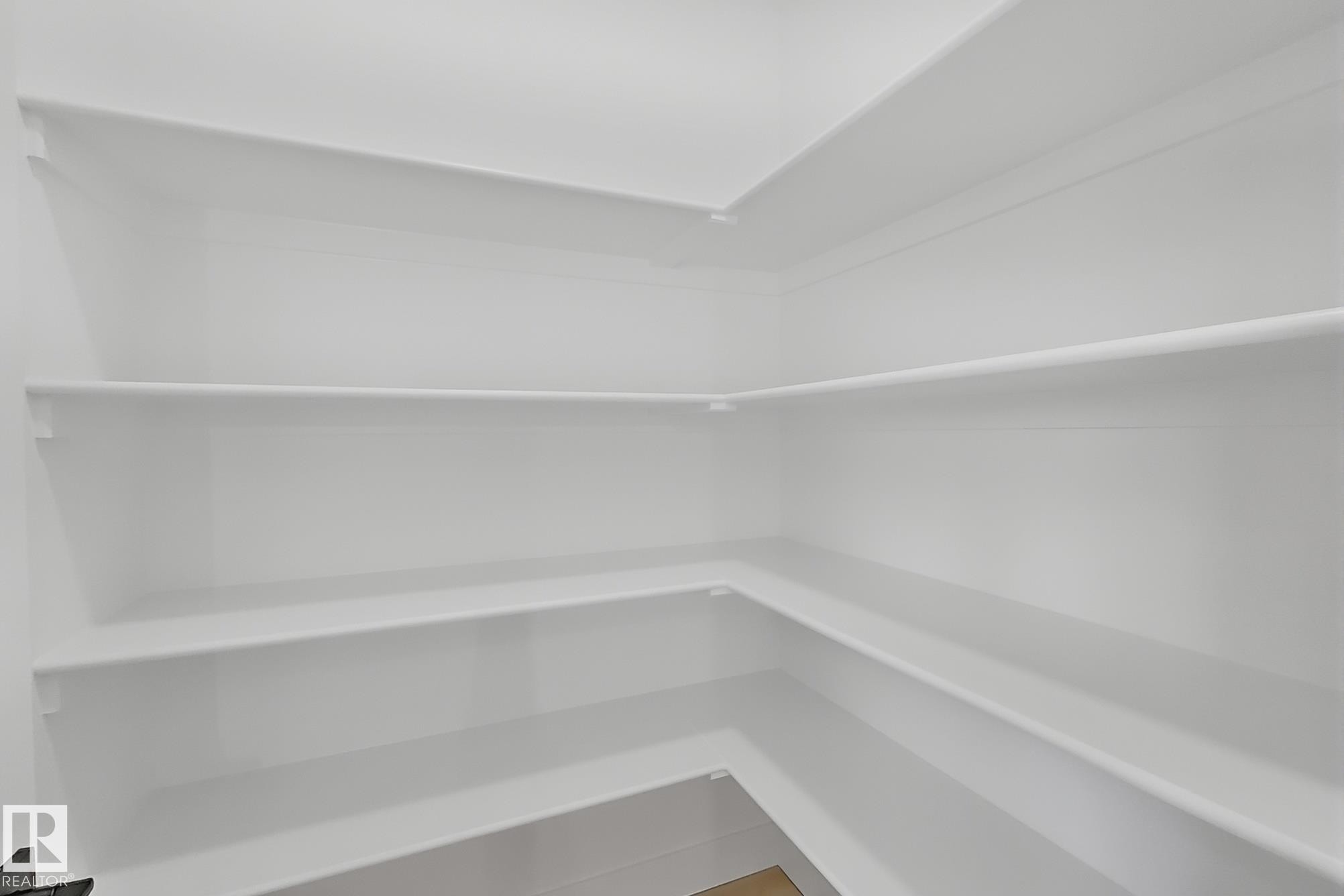 Walk-in pantry featuring multiple levels of white shelving, corner shelving units, and a light wood-finish floor - 4215 63 St, Beaumont, AB - Indoor With Storage