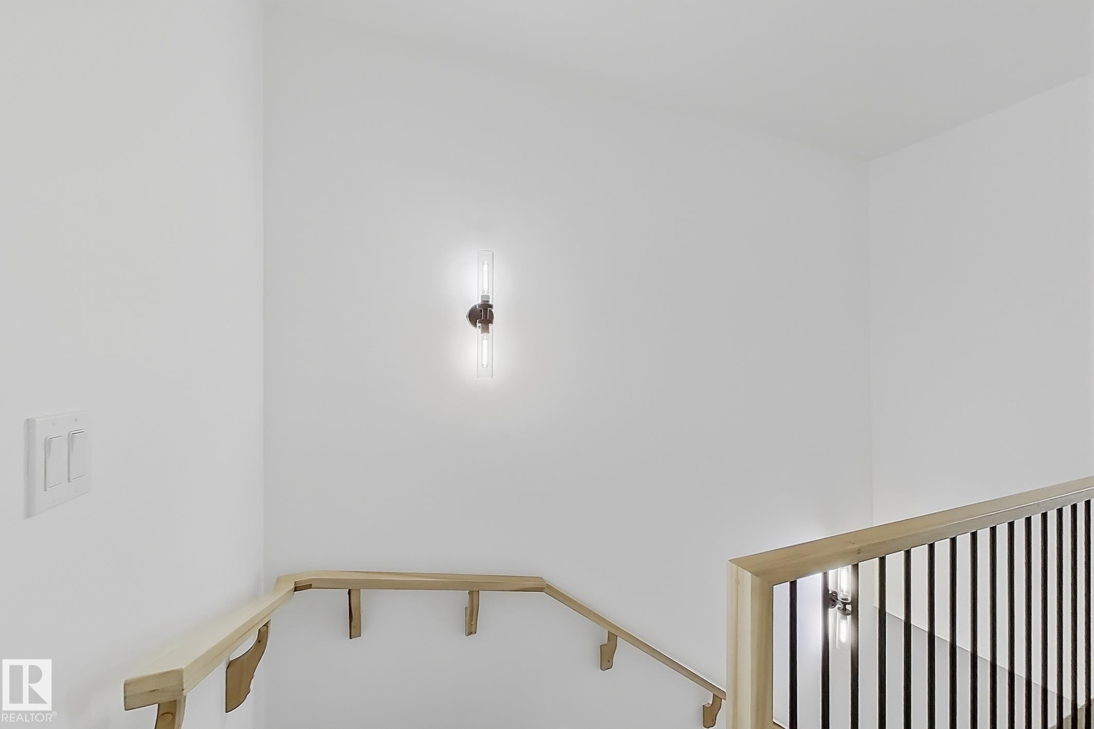 Bright interior space featuring a contemporary wall sconce, light wood-finish handrails, and a black wrought iron baluster system - 4215 63 St, Beaumont, AB - Indoor Photo Showing Other Room