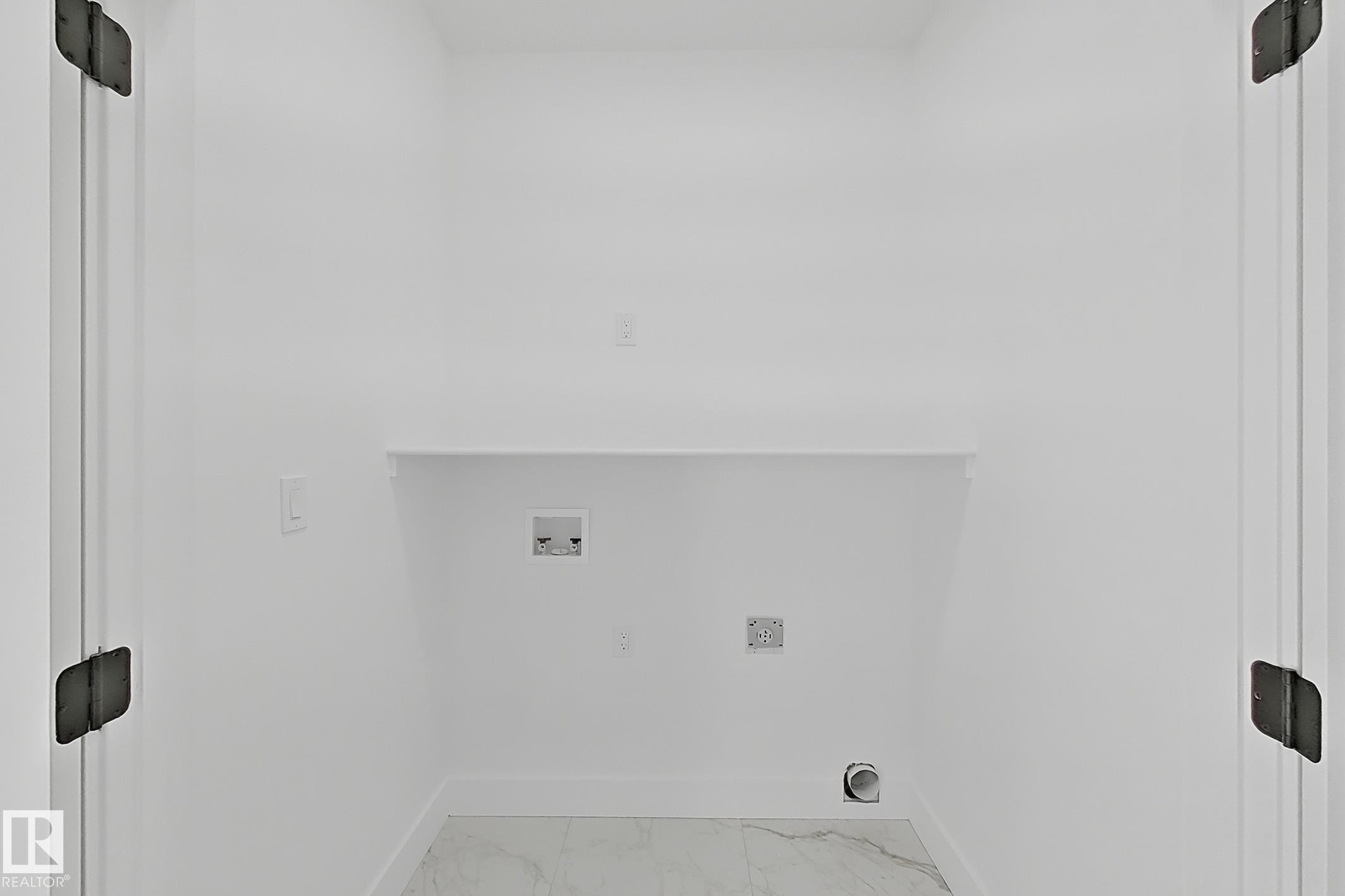 Dedicated laundry area featuring white walls, a built-in shelf, and marble-look floor tiling - 4215 63 St, Beaumont, AB -