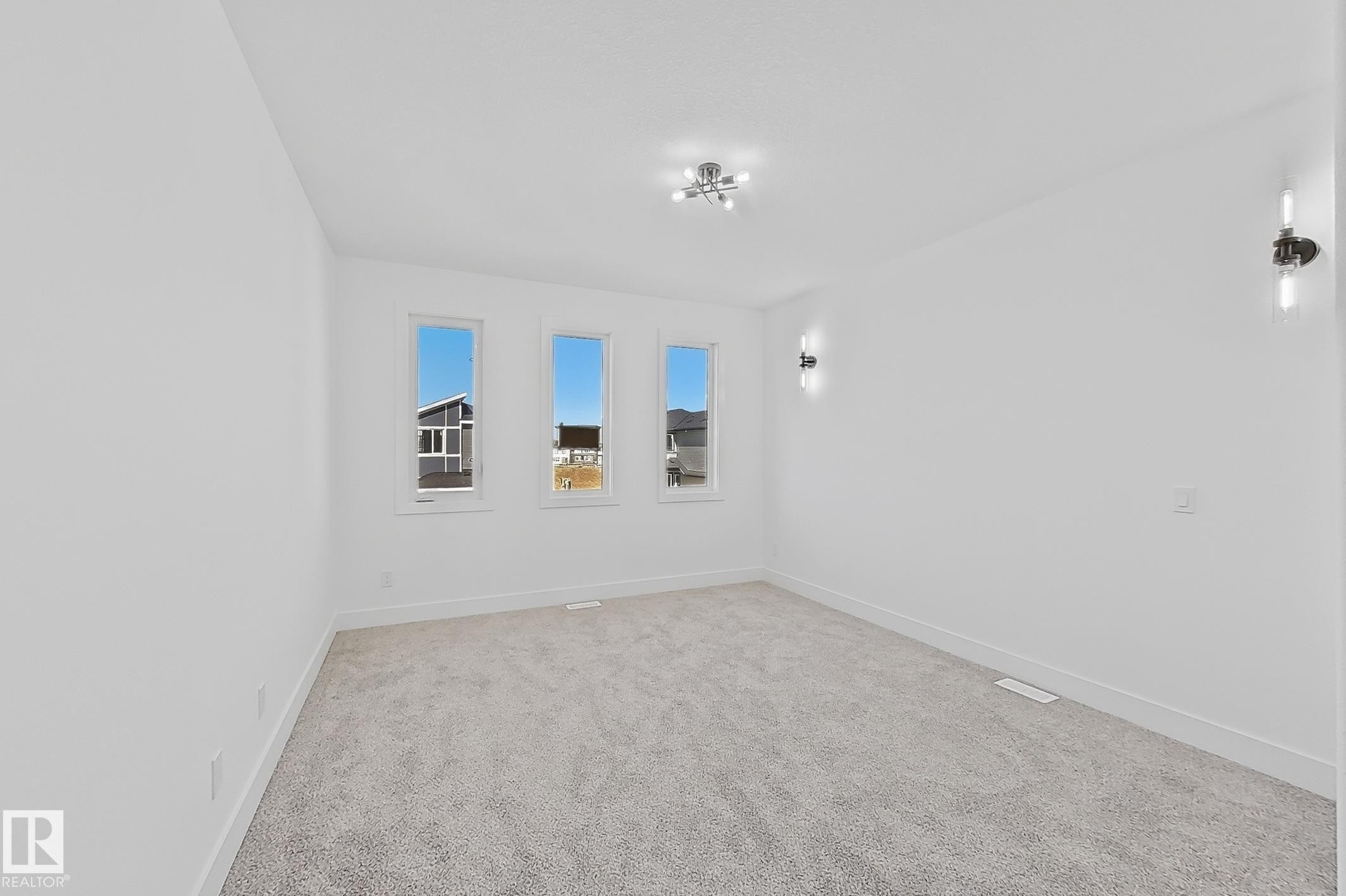 Room featuring three vertical windows, light gray carpeting, crisp white walls, white baseboards, a contemporary ceiling light fixture, and two wall sconces - 4215 63 St, Beaumont, AB - Indoor Photo Showing Other Room