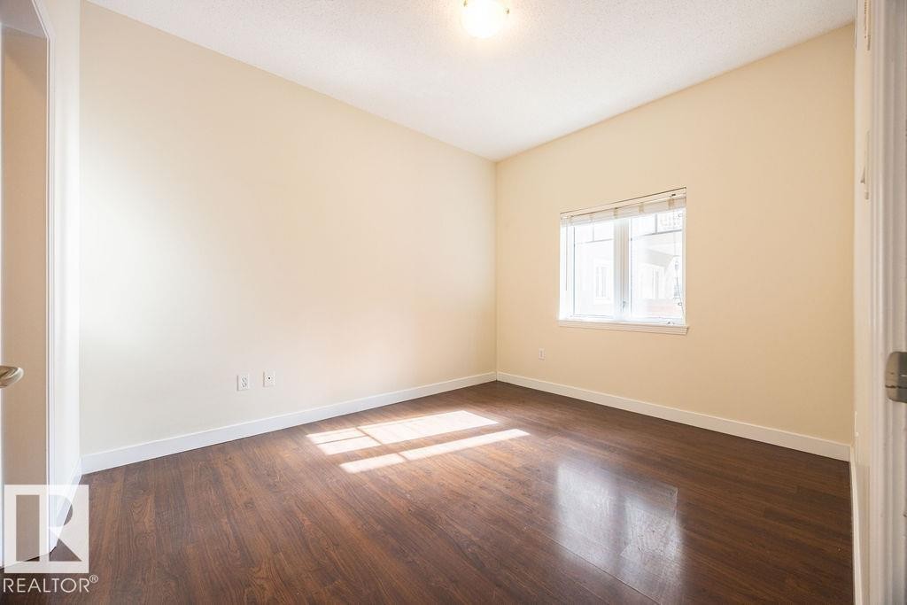Bright interior space featuring wood-finish flooring, light-toned walls, a window with horizontal blinds, and a flush-mount ceiling light fixture - #214 10333 112 St Nw, Edmonton, AB - Indoor Photo Showing Other Room