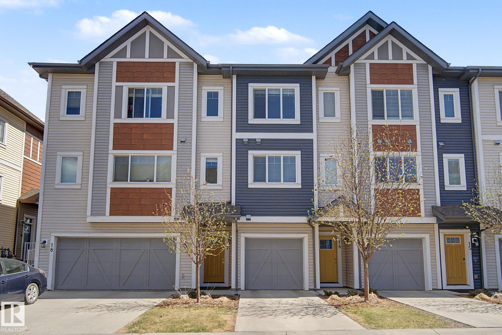Modern townhouse exterior featuring multi-toned siding, white trim, gabled roof accents, and an attached garage with a drive-up driveway - 17 320 Secord Boulevard, Edmonton, AB - Outdoor With Facade