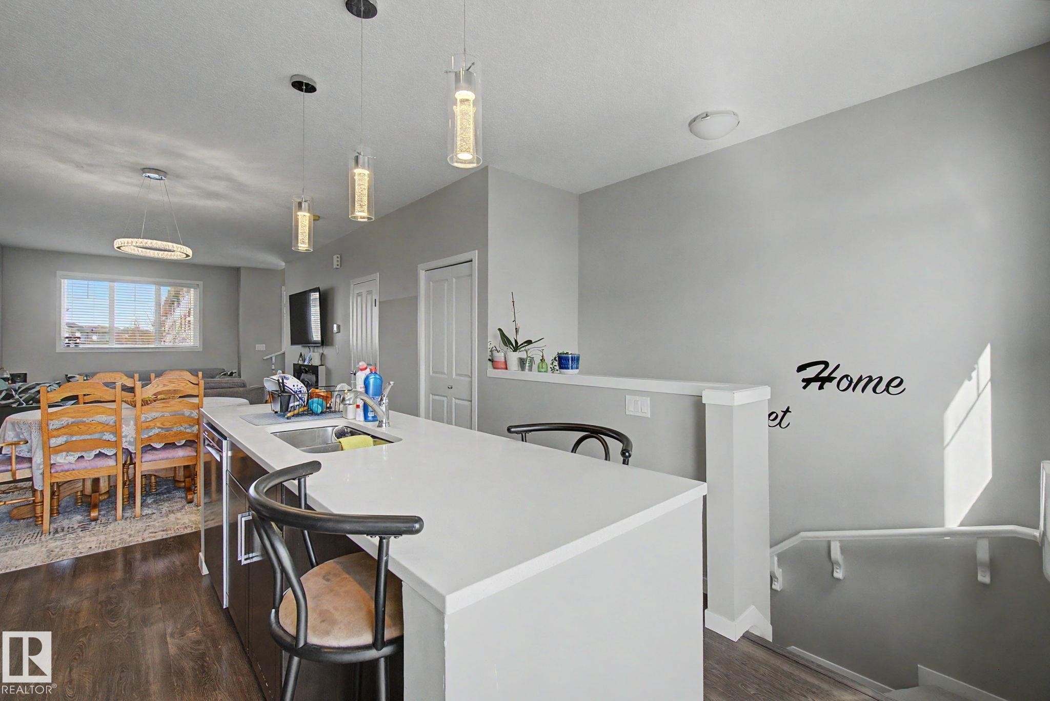 Kitchen island featuring a white countertop, undermount sink, and three pendant lights - 17 320 Secord Boulevard, Edmonton, AB - Indoor
