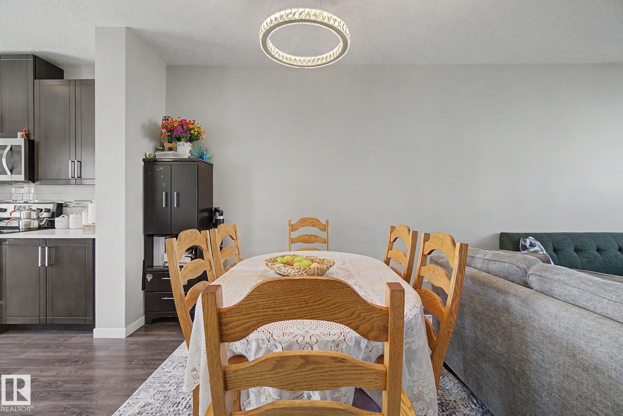 Open-concept dining area featuring a contemporary circular chandelier and wood-finish flooring - 17 320 Secord Boulevard, Edmonton, AB - Indoor Photo Showing Dining Room